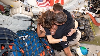 (April 7, 2026) – The Artemis II crew – (clockwise from left) Mission Specialist Christina Koch, Mission Specialist Jeremy Hansen, Commander Reid Wiseman, and Pilot Victor Glover – take time out for a group hug inside the Orion spacecraft on their way home. Following a swing around the far side of the Moon on April 6, 2026, the crew exited the lunar sphere of influence (the point at which the Moon's gravity has a stronger pull on Orion than the Earth's) on April 7, and are headed back to Earth for a splashdown in the Pacific Ocean on April 10. The crew was selected in April 2023, and have been training together for their mission for the past three years.