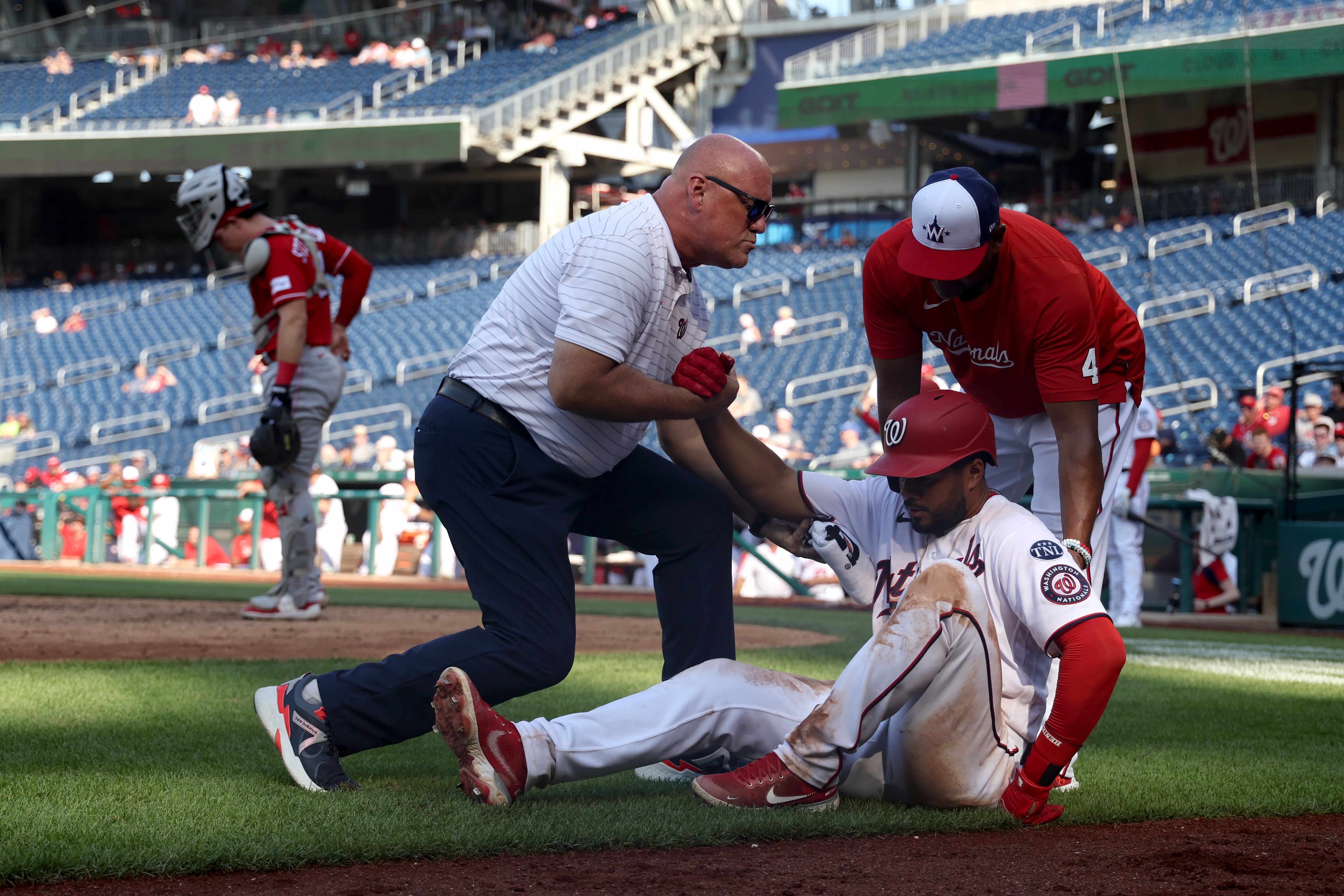 Trainer Paul Lessard and manager Dave Martinez help Jeimer Candelario of the Nationals get up after he was hit by a pitch in the 10th inning of Washington's 10-inning loss to the Reds on Thursday.