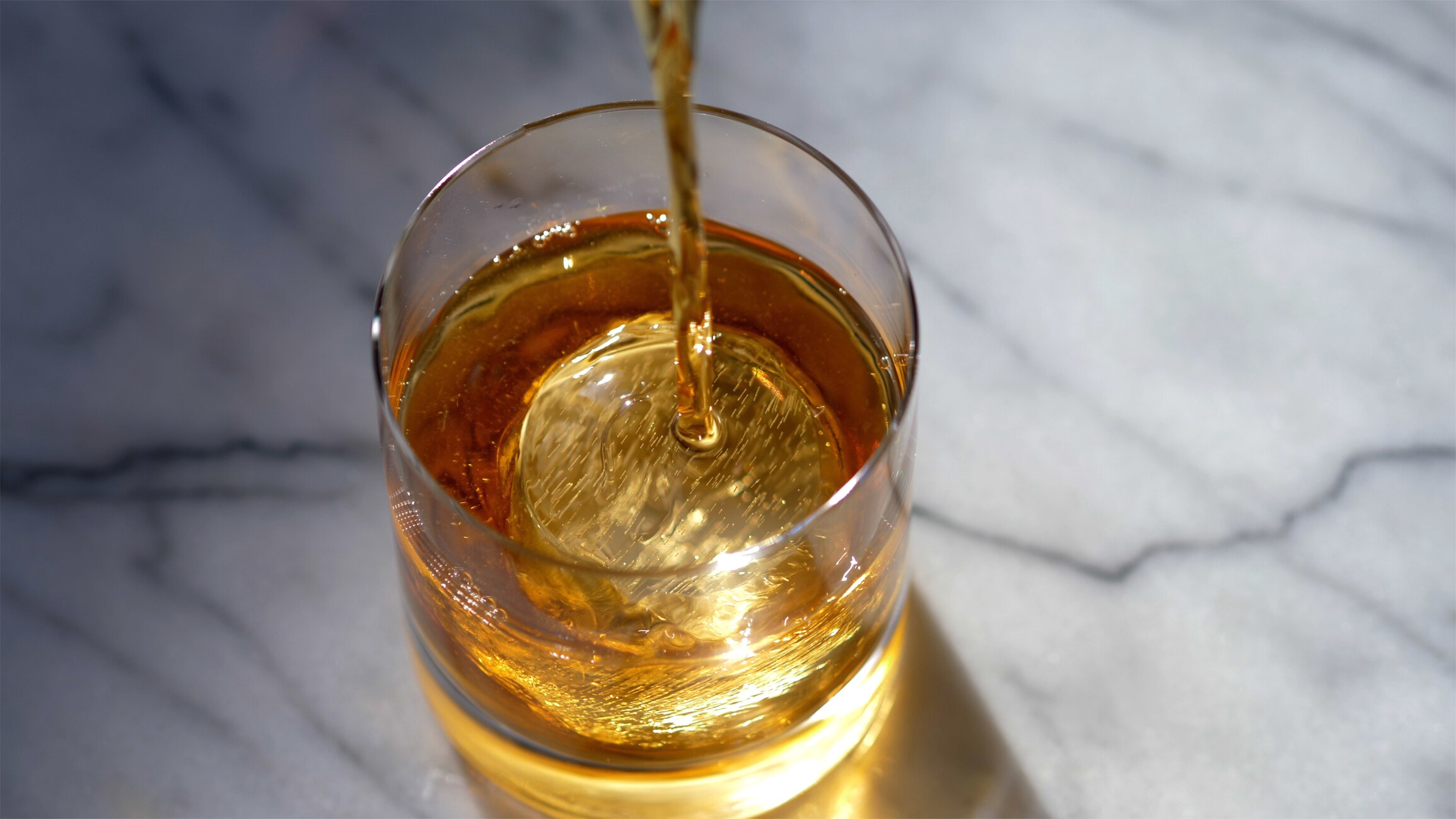 Rye poured over ice cube from above, being stirred.