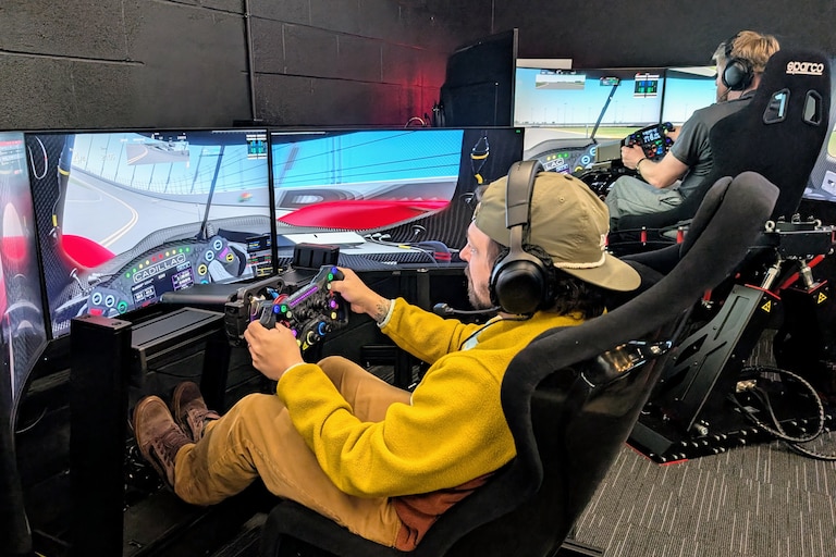 Bryce Swarm, left, and JP Dwyer run a demonstration race in two of the cockpits at PS1 Sim Racing Annapolis. The rigs rely on a computer physics generator to match the use of steering wheels and pedals to images on the screen, sounds and motions.