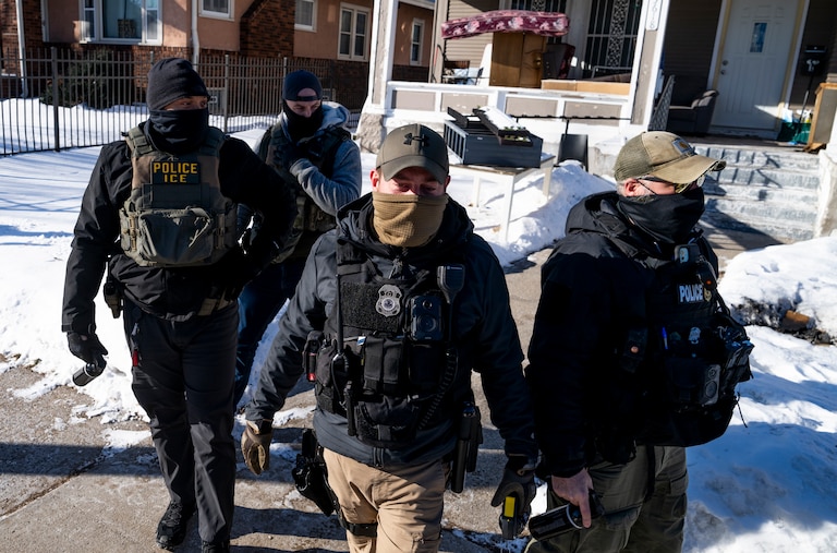 A group of four men wearing law enforcement gear and masks walk on a sidewalk toward the camera.