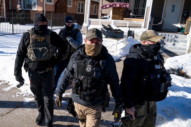 A group of four men wearing law enforcement gear and masks walk on a sidewalk toward the camera.