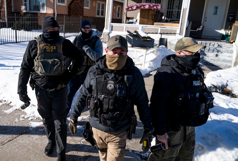 A group of four men wearing law enforcement gear and masks walk on a sidewalk toward the camera.