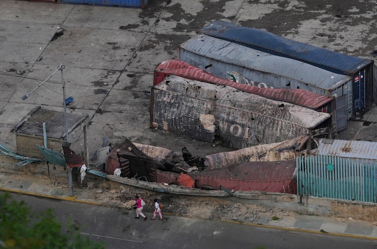 Pedestrians walk past destroyed containers at La Guaira port after explosions were heard in Venezuela, Saturday, Jan. 3, 2026.