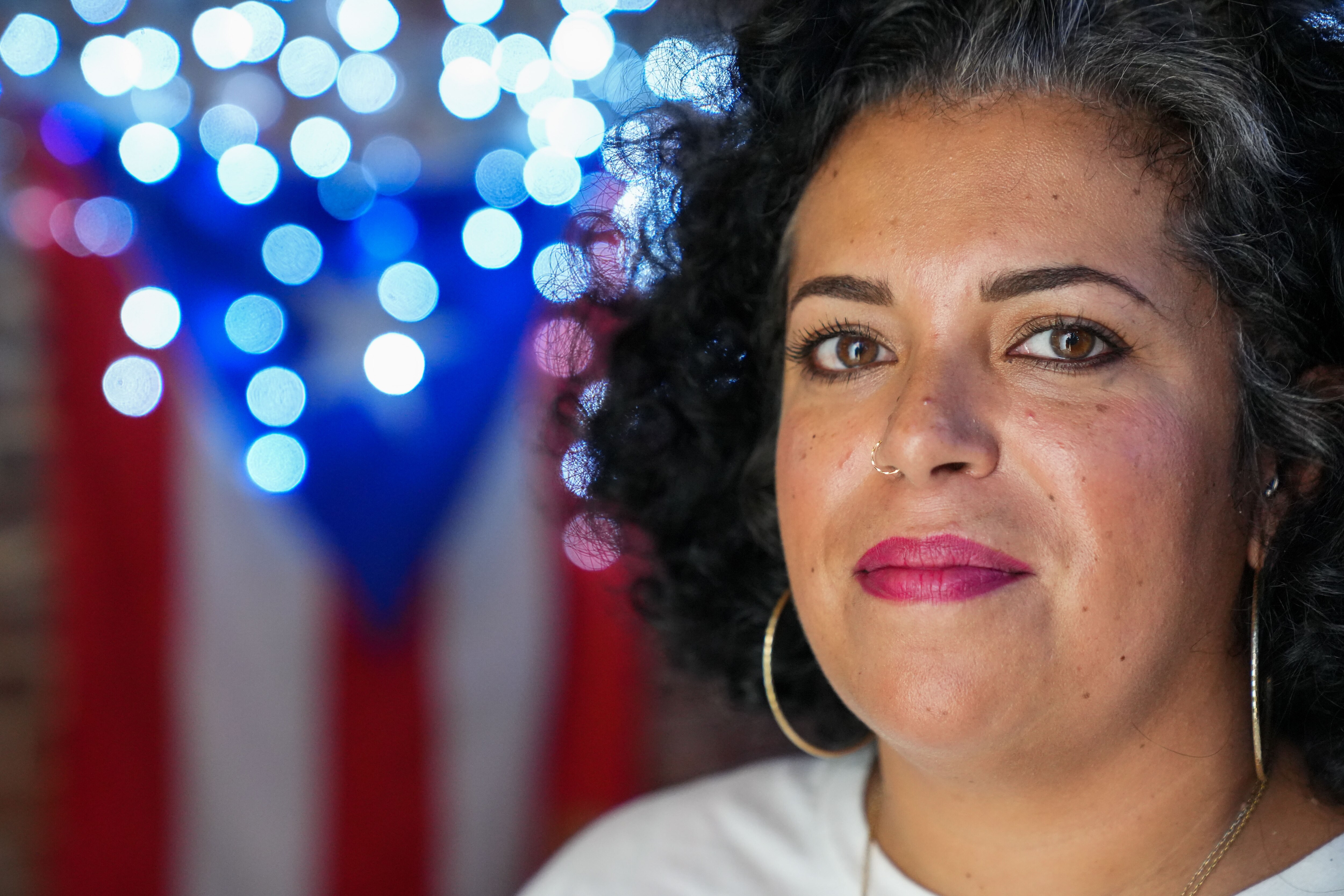 Cristina Delgado stands for a portrait on 9/7/22 in front of a lit up Puerto Rican flag inside of the museum and cultural hub she curated inside her home.
