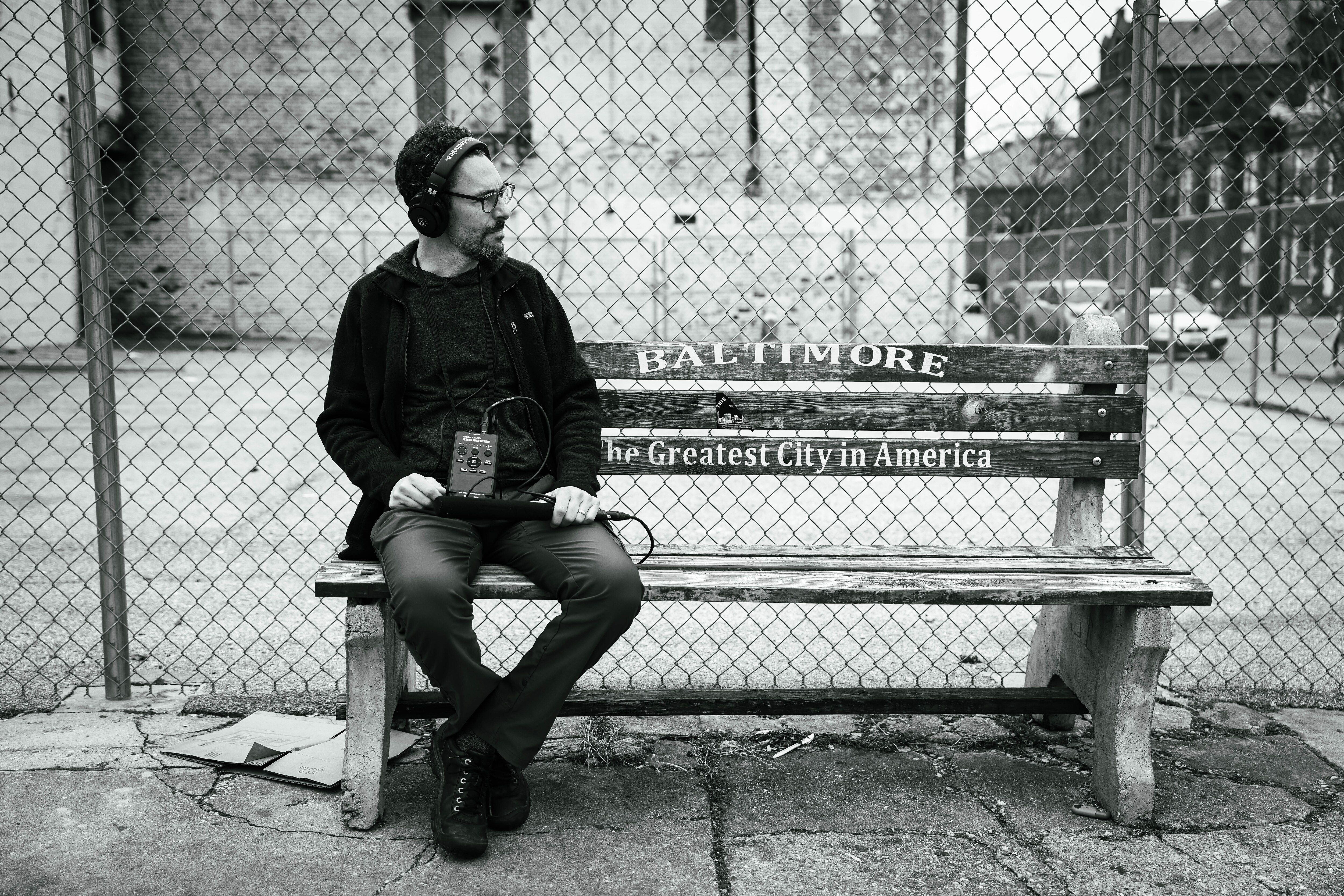 Aaron Henkin of WYPR sits on a bench in boasting Martin O'Malley's slogan: "Baltimore - The Greatest City in America" in Federal Hill.