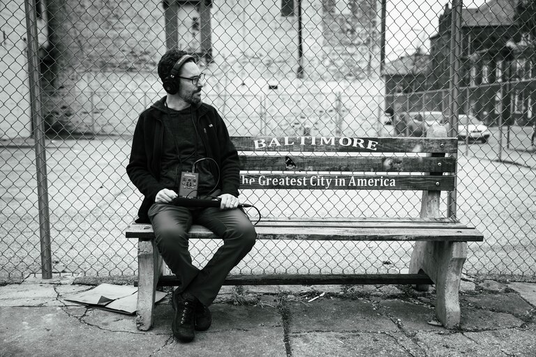 Aaron Henkin of WYPR sits on a bench in boasting Martin O'Malley's slogan: "Baltimore - The Greatest City in America" in Federal Hill.