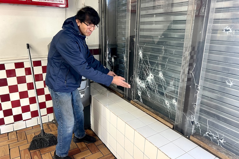 Hameed Dulah shows bullet holes in his storefront's windows after a shooting the night before at NY Chicken Fish and Grill.
