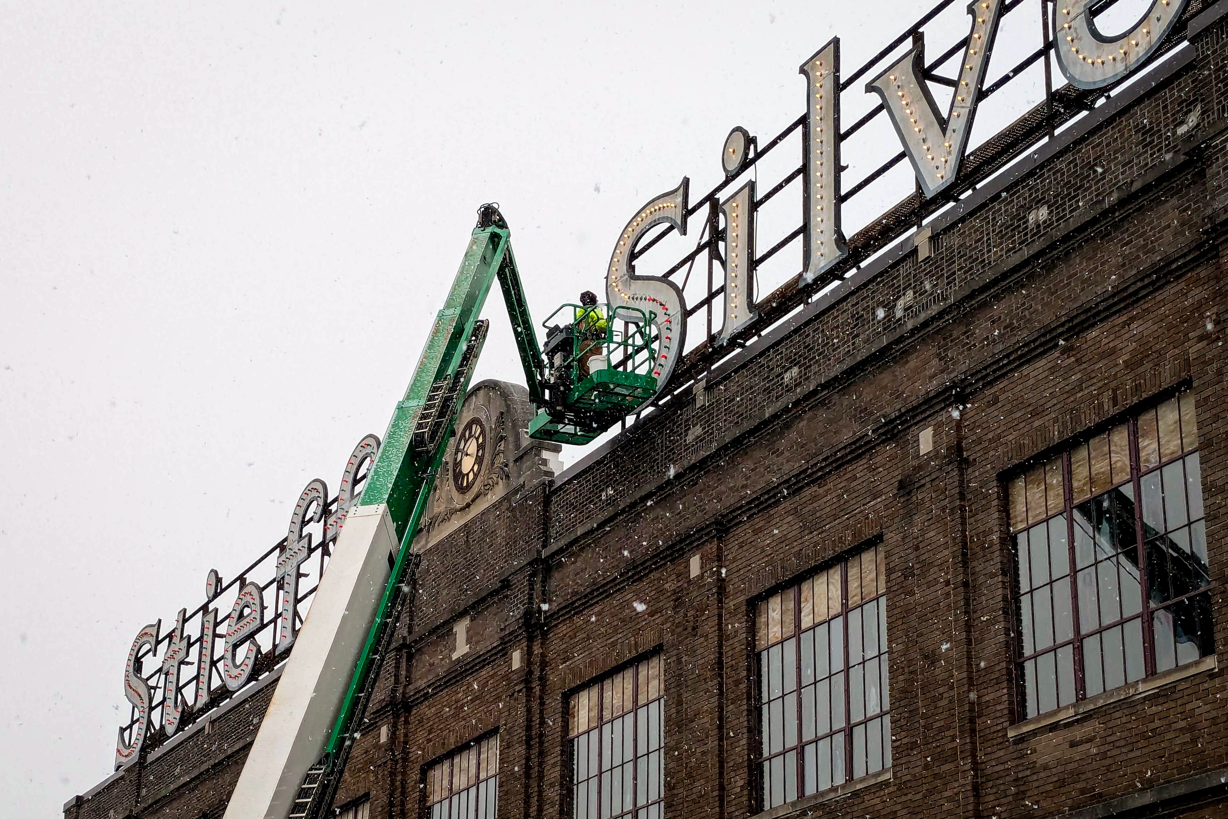 A worker changes the lights on the Stieff Silver sign to Christmas colors as the first snow falls in Baltimore on Friday, December 5, 2025.