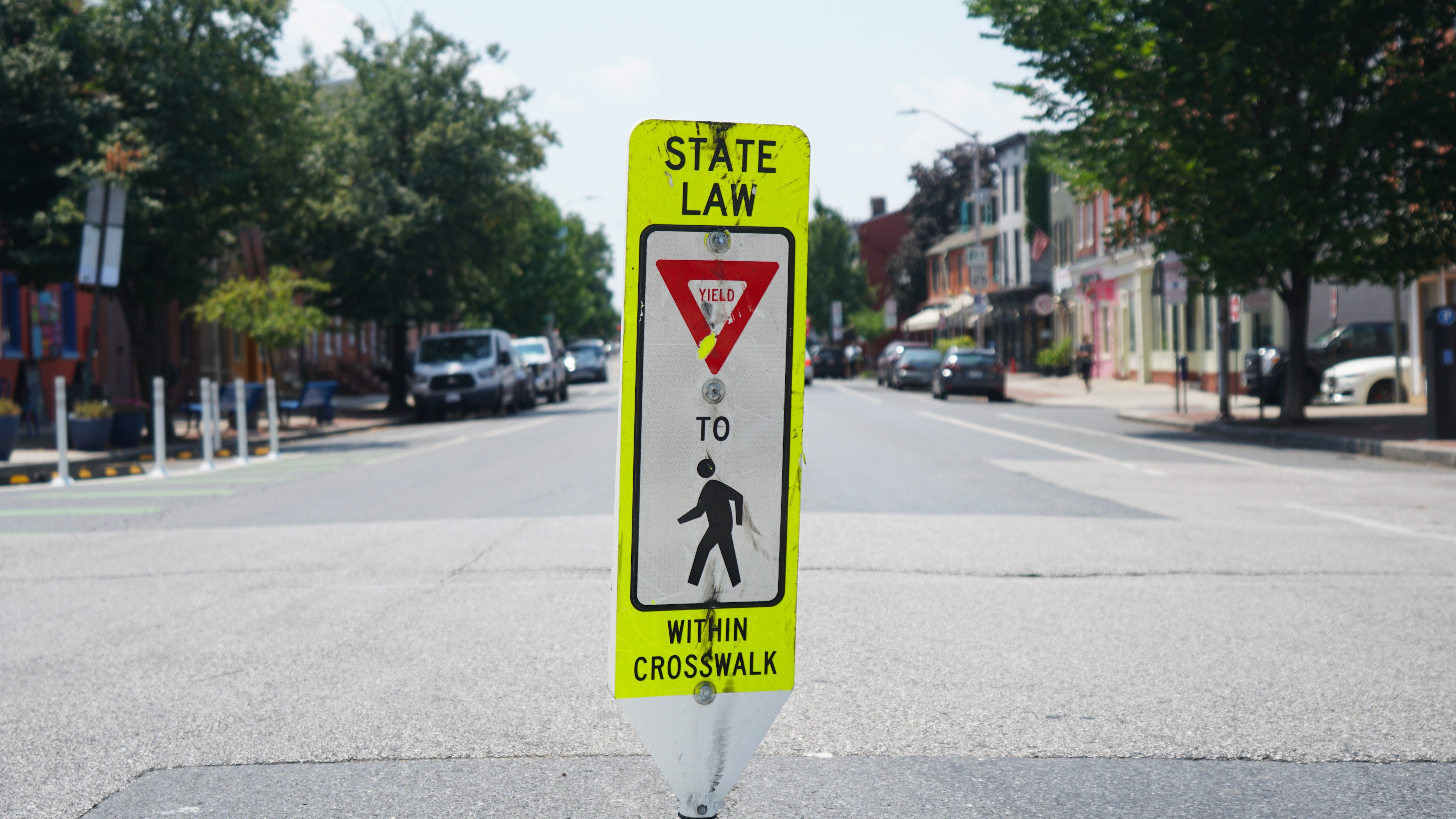 A close up photo of a yellow crosswalk sign at a city intersection.