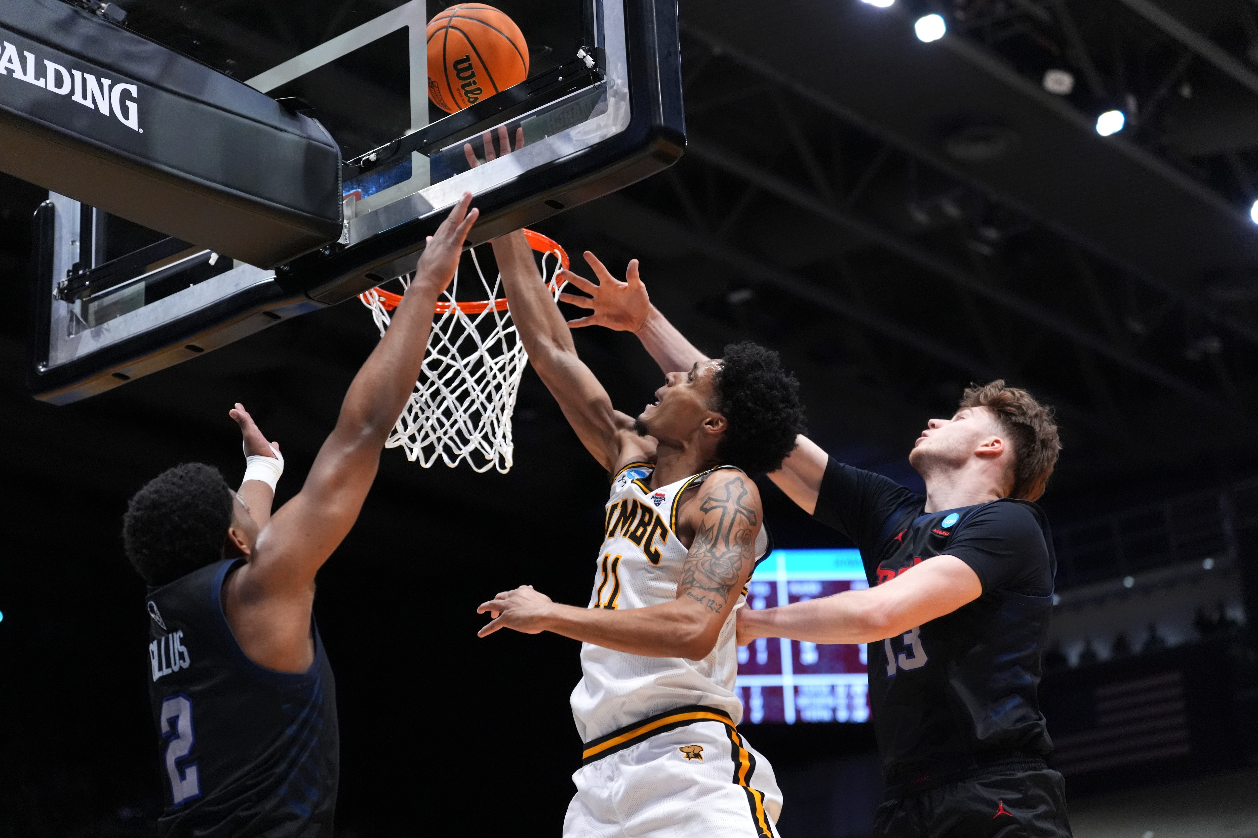 UMBC forward Caden Diggs (11), center, scores at the basket as Howard guard Cam Gillus (2), left, and center Danas Kazakevicius (13), right, defend during the first half.