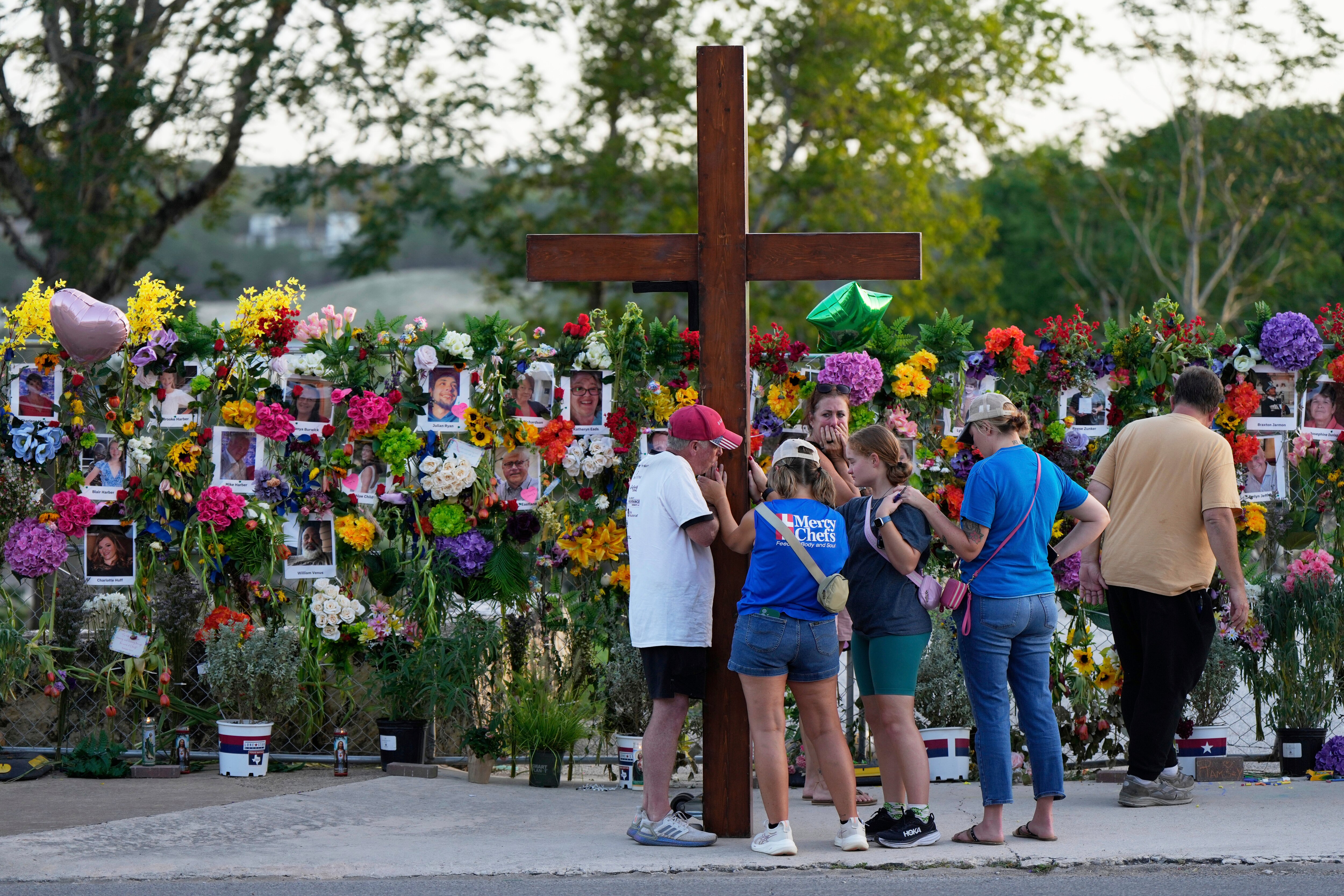 Dan Beazley, left, holds a large cross as he prays with visitors at a memorial for flood victims on Thursday, July 10, 2025, in Kerrville, Texas.