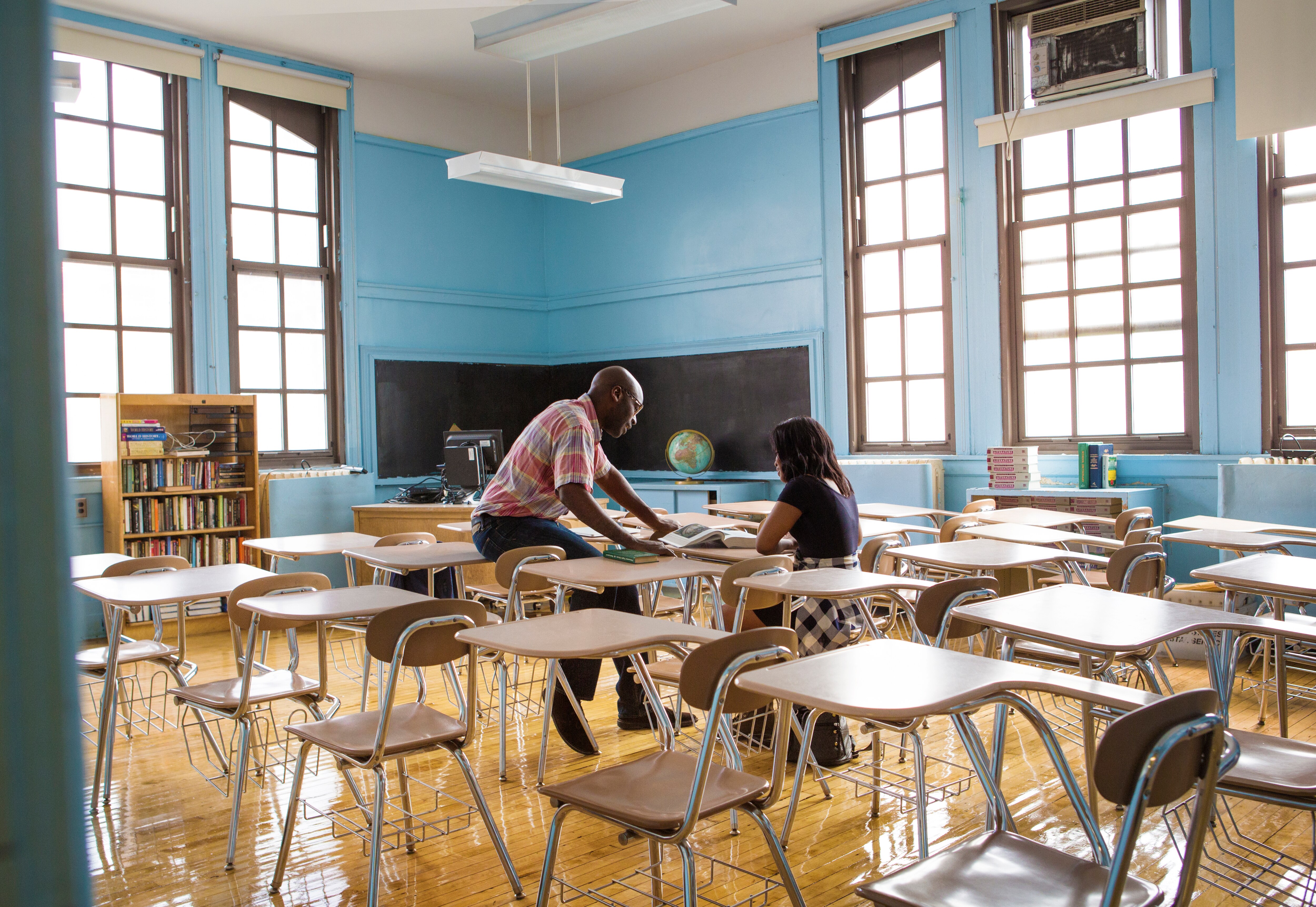 Male tutor listening to female student reading in empty class