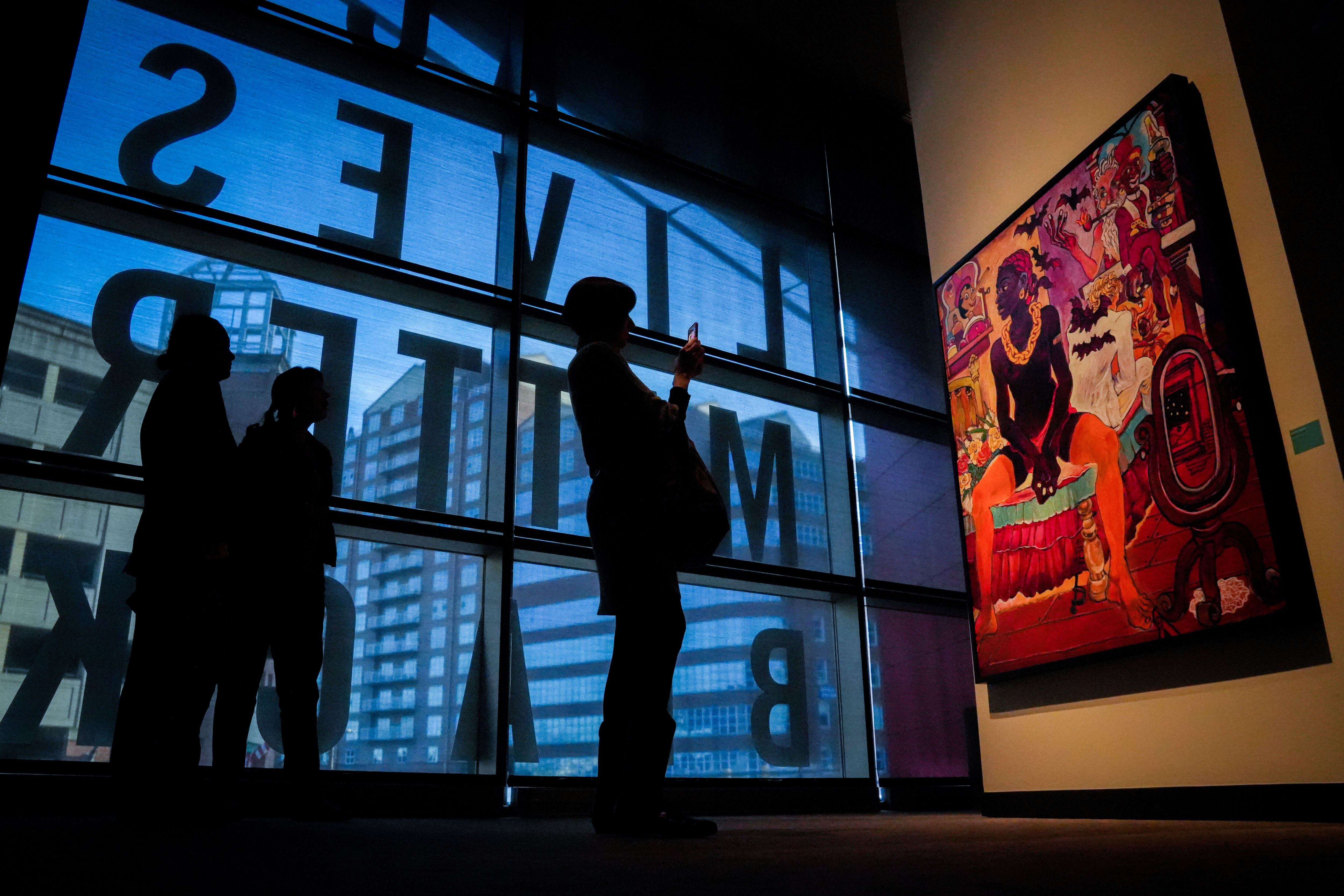Visitors to the Reginald F. Lewis Museum take photos and examine a piece of art entitled “Cupid and Psyche” by Arvie Smith in the “Afro-Futurist Manifesto: Blackness Reimagined” exhibit on March 16, 2023.