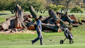 A golfer walks near log sections cut from trees at the East Potomac Golf Links, in Washington, Tuesday, Oct. 13, 2026.