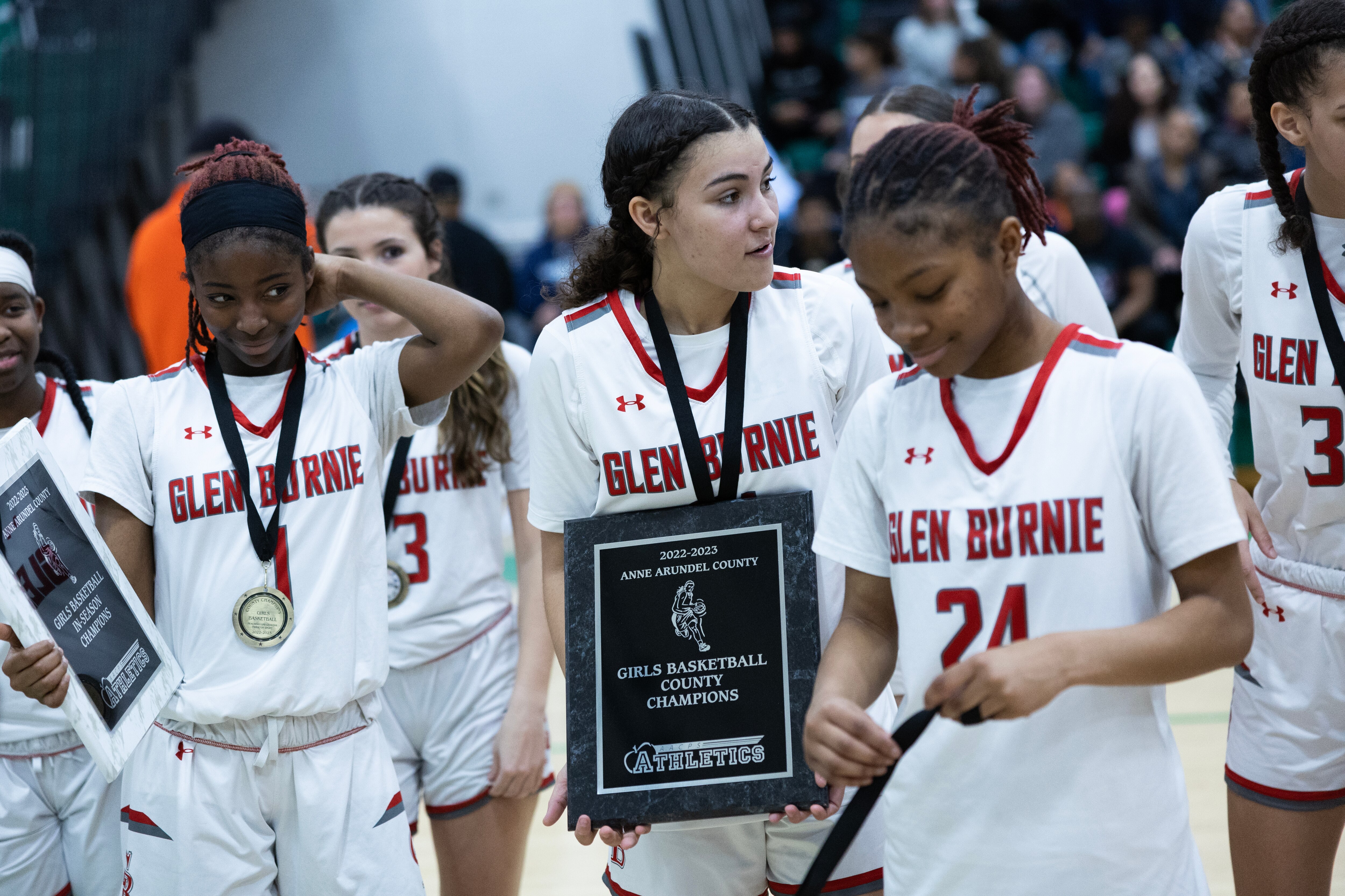 Glen Burnie players celebrate with medals and a team trophy following the Anne Arundel County Girls Basketball Championship game in Odenton, Md., on Saturday, February 18, 2023. Glen Burnie defeated Severna Park 37-34 in regulation time. (Tom Brenner for The Baltimore Banner)