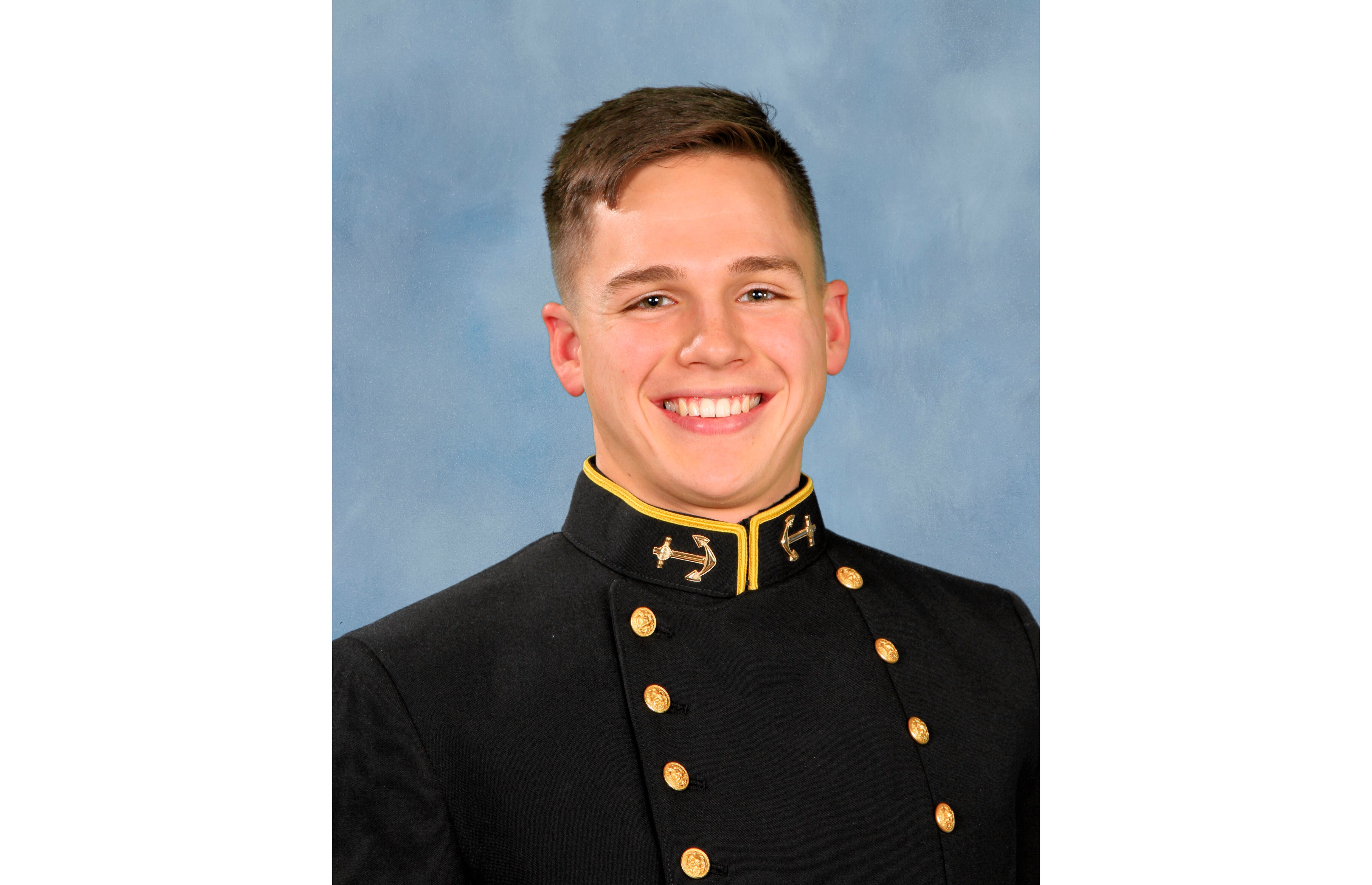 Portrait photo of Luke Bird, a young white man, smiling in formal uniform for U.S. Naval Academy against a blue background.