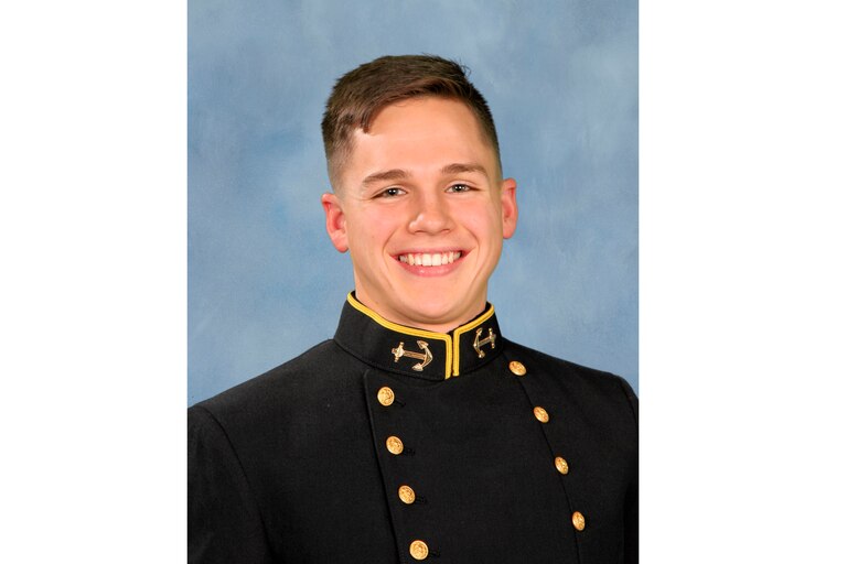 Portrait photo of Luke Bird, a young white man, smiling in formal uniform for U.S. Naval Academy against a blue background.