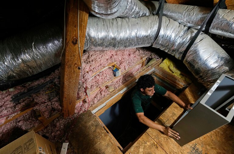 FILE - An installer climbs into an attic with parts of a new HVAC system that was installed in a residential home in Fate, Texas, on Wednesday, July 30, 2025