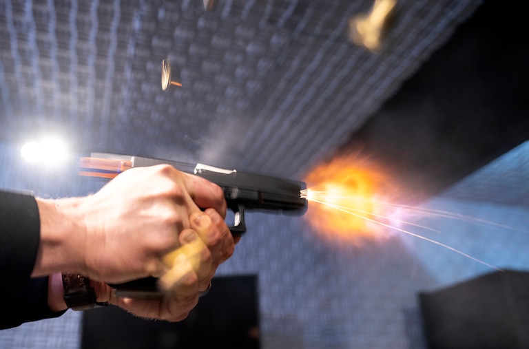 A semi-automatic pistol with a conversion device installed making it fully automatic is fired as four empty shell casings fly out of the weapon