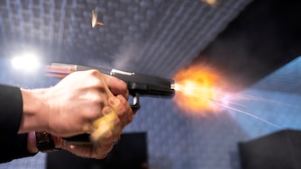 A semi-automatic pistol with a conversion device installed making it fully automatic is fired as four empty shell casings fly out of the weapon