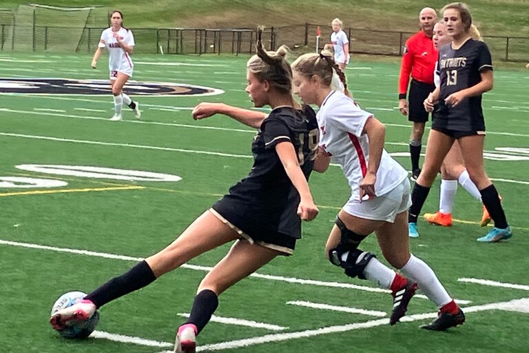 John Carroll junior defender Caroline Harrison attempts to clear the ball while being pressured by Mercy senior forward Brooke Hunter in a showdown for the top seed in the upcoming IAAM A Conference playoffs. The third-ranked Magic toppled the No. 1 Patriots, 2-0, to earn a first-round postseason bye.
