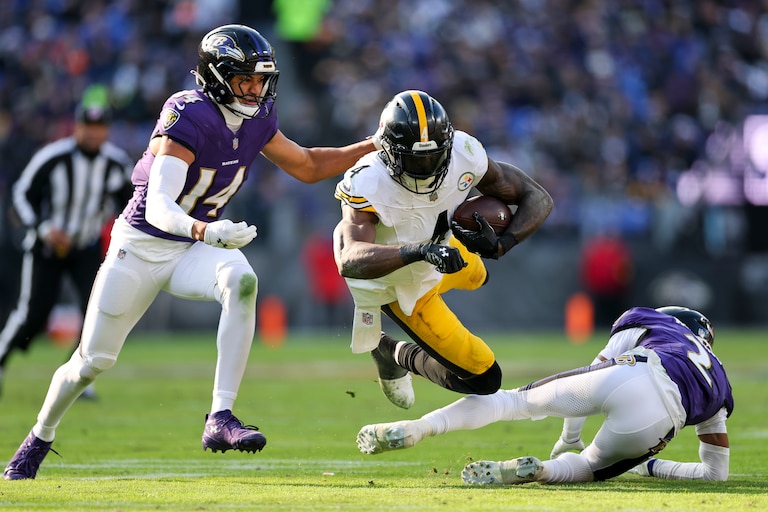 BALTIMORE, MARYLAND - DECEMBER 07: DK Metcalf #4 of the Pittsburgh Steelers is tackled by Nate Wiggins #2 and Kyle Hamilton #14 of the Baltimore Ravens during the second quarter at M&T Bank Stadium on December 7, 2025 in Baltimore, Maryland.