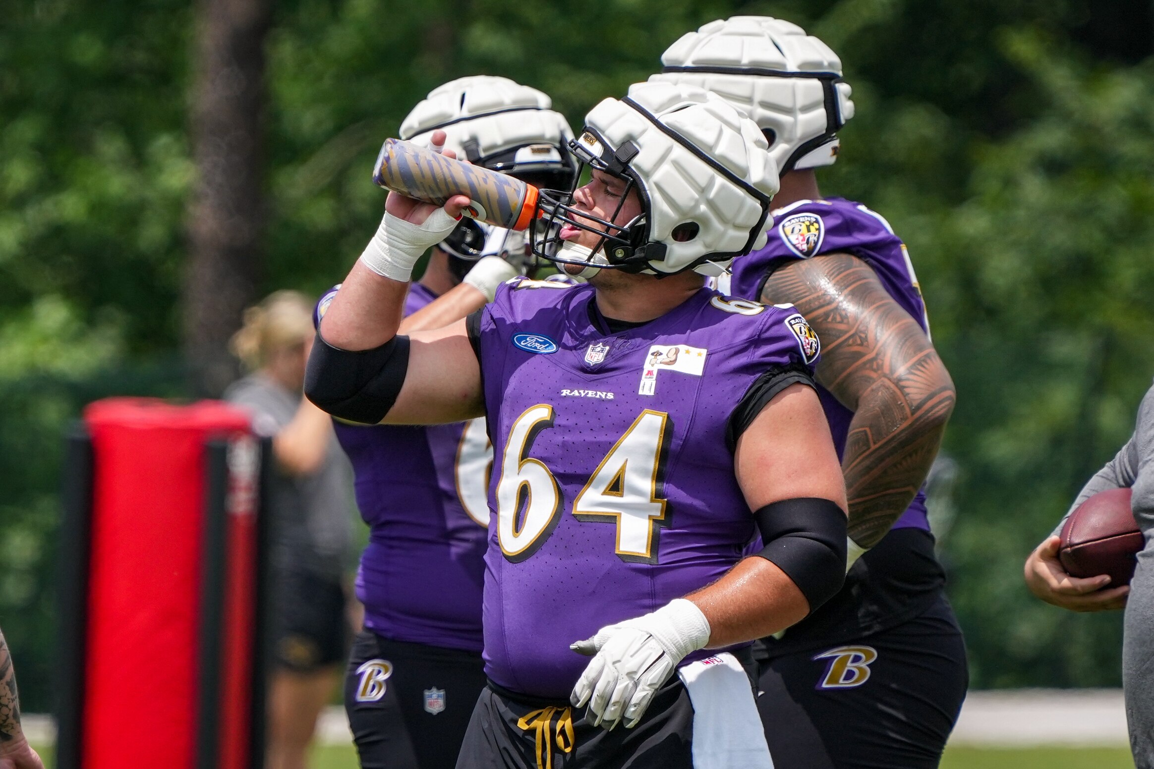 Baltimore Ravens center Tyler Linderbaum (64) rehydrates before starting a new drill during the team’s 2024 training camp at the Under Armour Performance Center in Owings Mills, Maryland, on Tuesday, July 23, 2024.