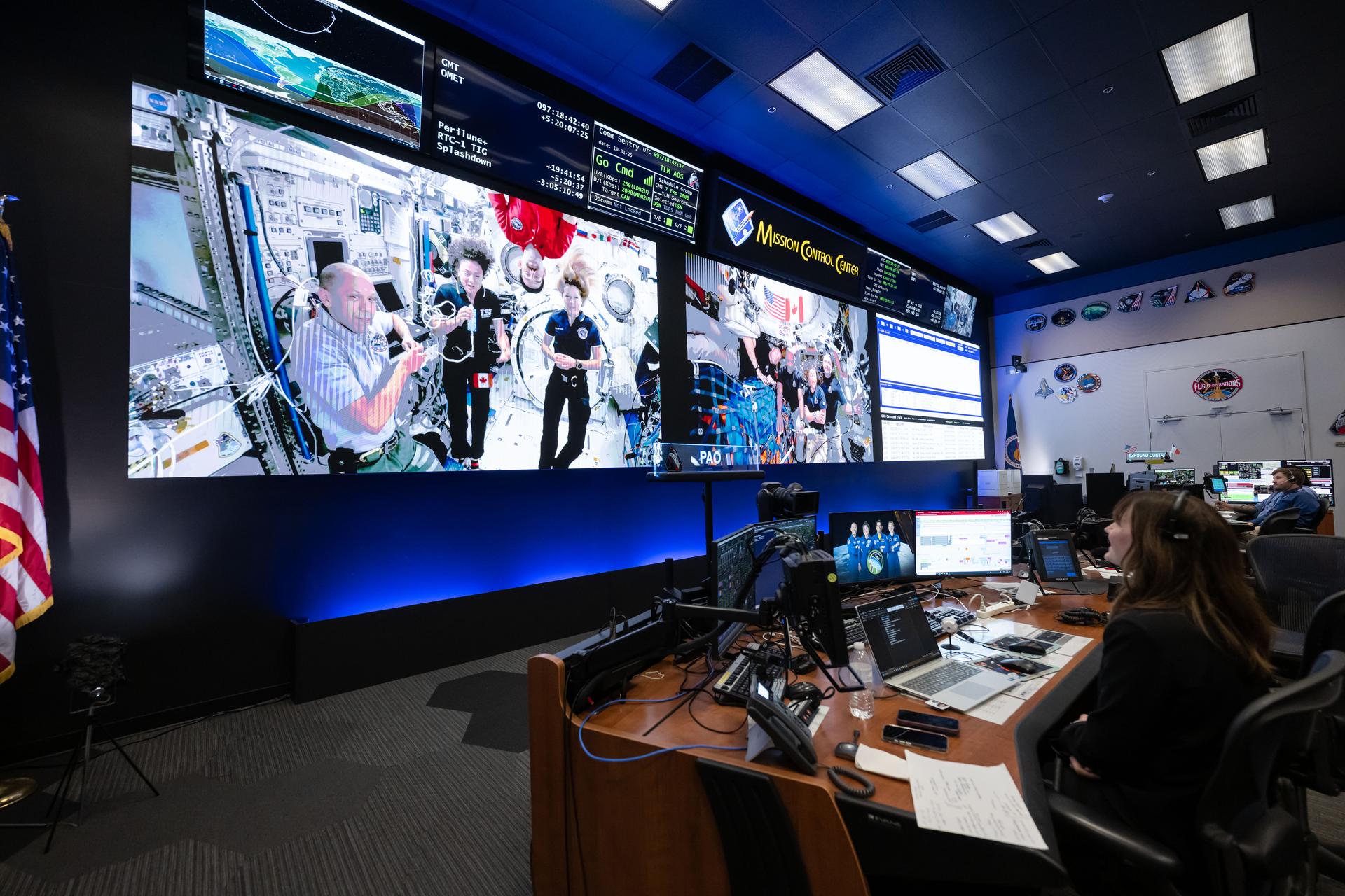 (April 7, 2026) - Members of the International Space Station Expedition 74 (left) and Artemis II (right) crews are seen at once on the screens inside the International Space Station flight control room in Mission Control at NASA's Johnson Space Center in Houston. The two crews connected in a 15-minute ship-to-ship call on April 7, 2026, while the Artemis II crew was on its way back from the Moon.