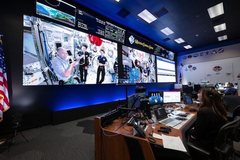 (April 7, 2026) - Members of the International Space Station Expedition 74 (left) and Artemis II (right) crews are seen at once on the screens inside the International Space Station flight control room in Mission Control at NASA's Johnson Space Center in Houston. The two crews connected in a 15-minute ship-to-ship call on April 7, 2026, while the Artemis II crew was on its way back from the Moon.