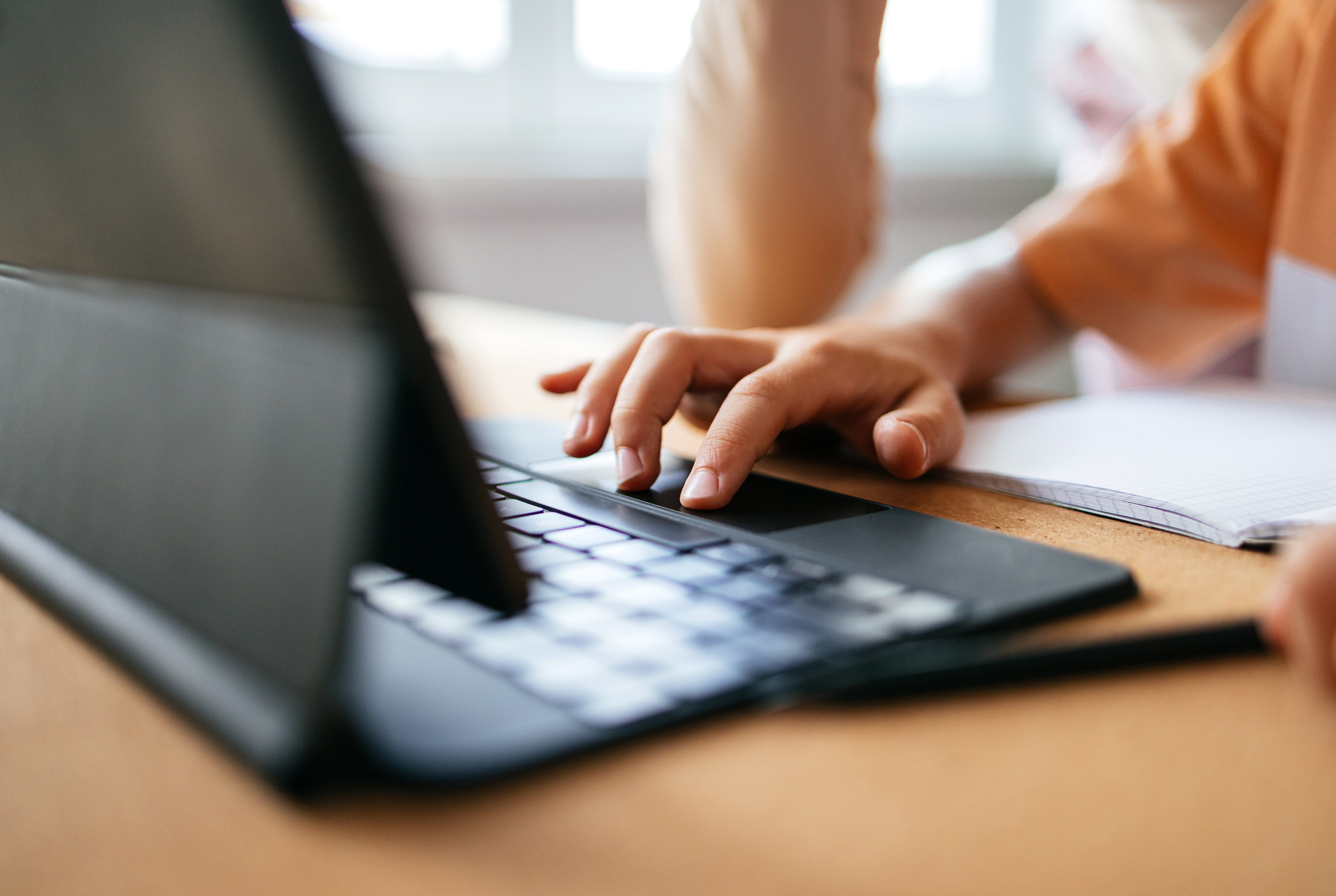 Zoomed in photo of a young boy's hand using the tablet and typing something on the keyboard.