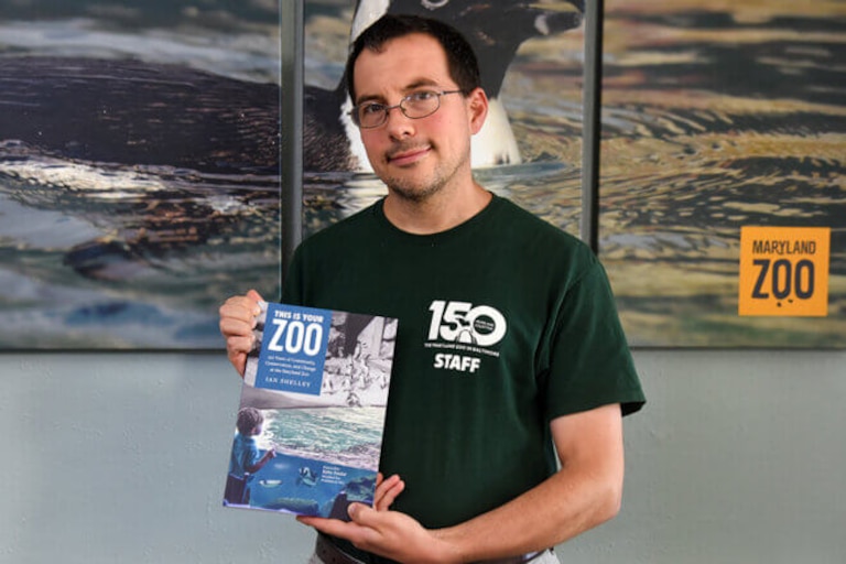Ian Shelley holds a copy of his newly published book, “This Is Your Zoo: 150 Years of Community, Conservation, and Change at the Maryland Zoo.” Shelley is the zoo's registrar.