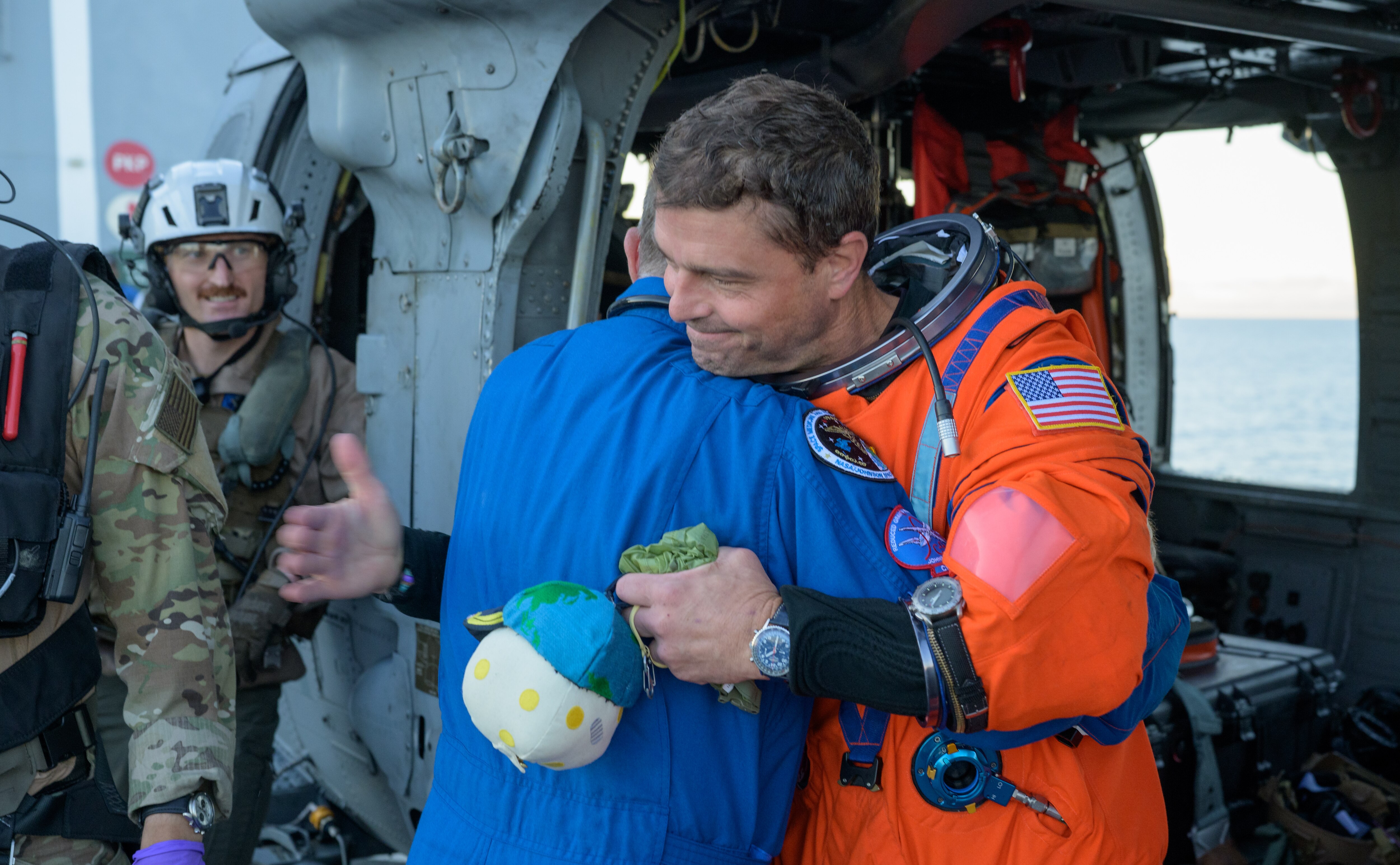 NASA astronaut Reid Wiseman, Artemis II commander, gives NASA Flight Surgeon Richard Scheuring a hug next to a Navy MH-60 Seahawk from Helicopter Sea Combat Squadron (HSC) 23 on the flight deck of USS John P. Murtha after he and fellow crewmates NASA Astronauts Victor Glover, Christina Koch, and CSA (Canadian Space Agency) astronaut Jeremy Hansen, were extracted from their Orion spacecraft after splashdown, Friday, April 10, 2026, in the Pacific Ocean off the coast of California. NASA’s Artemis II mission took the quartet on a nearly 10-day journey around the Moon and back to Earth. Following a splashdown at 5:07 p.m. PDT (8:07 p.m. EDT), NASA, U.S. Navy, and U.S. Air Force teams are working to bring the Orion spacecraft aboard the recovery ship. Photo Credit: (NASA/Bill Ingalls)
