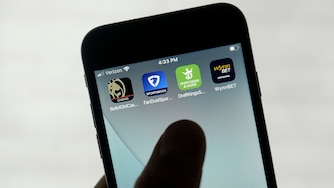 A hand hold a mobile phone with four sports betting apps displayed.