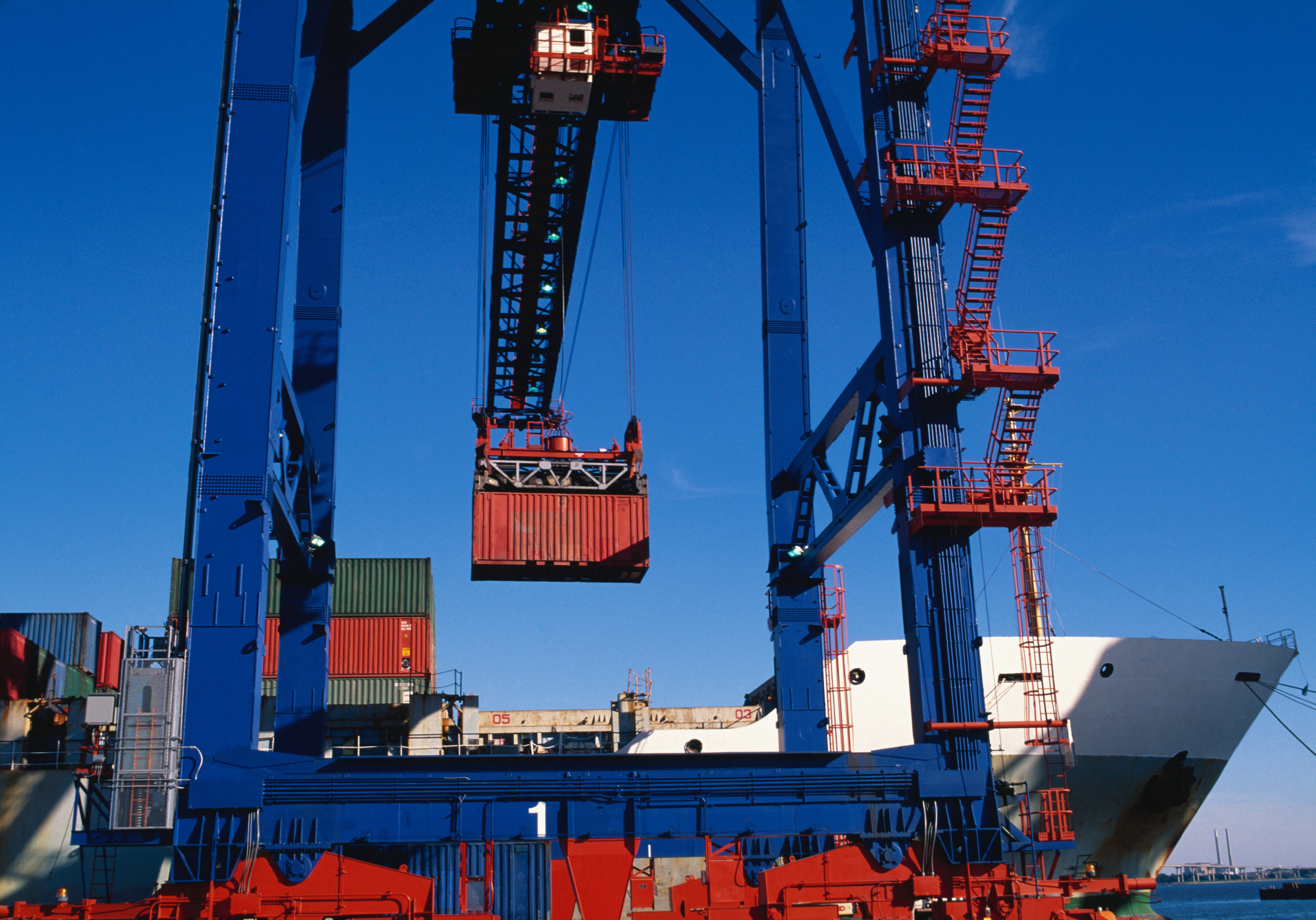 A blue crane loads a red container onto a cargo ship at the Port of Baltimore.