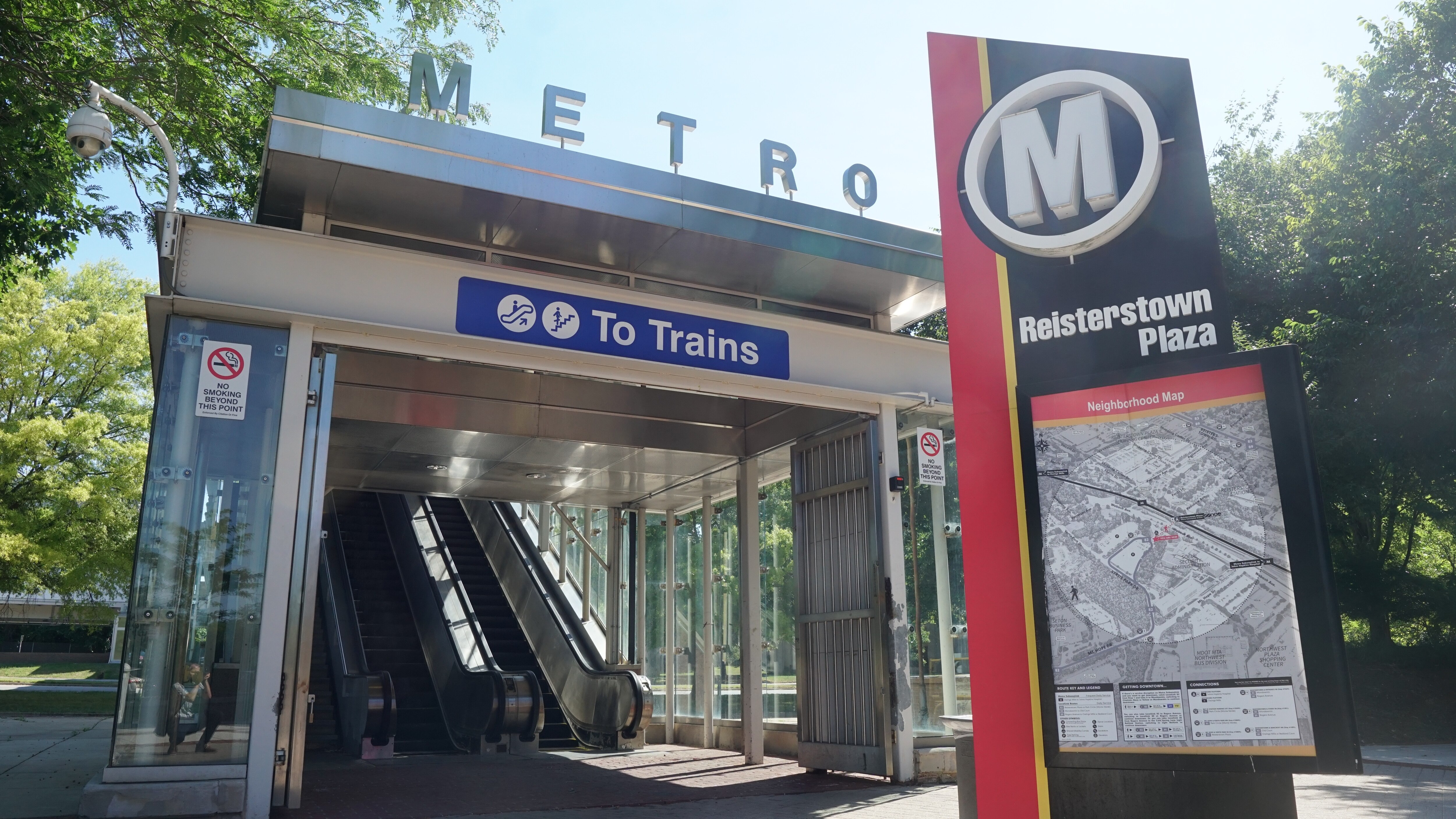 Two escalators inside a small structure that says "METRO" at the top with a black and red vertical sign out front indicating it is located at Reisterstown Plaza.