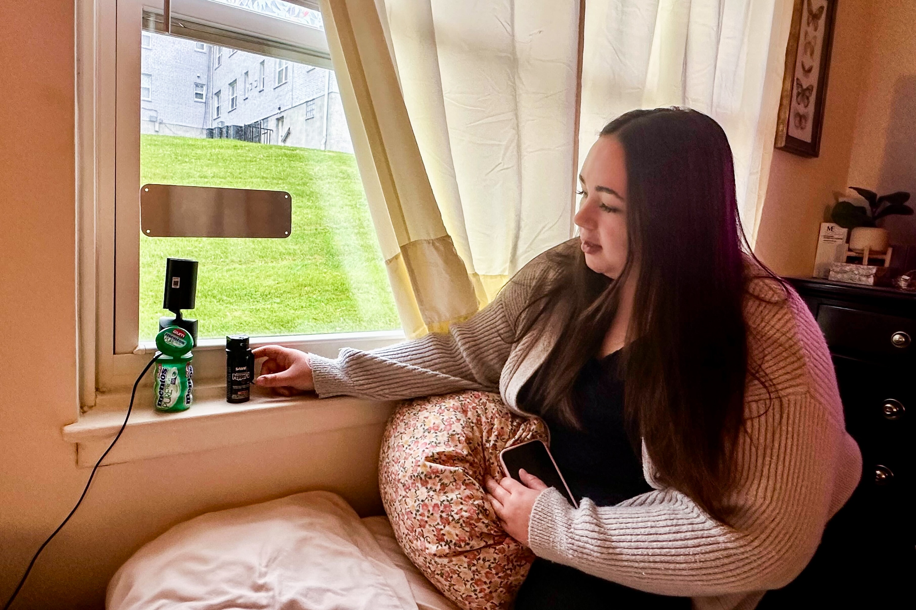 Devin Kaestner shows off one the Ring cameras, propped up by a bottle of gum, that she and her roommates installed in each of their bedroom windows to ward off "peeping Toms," in their first-floor Towson apartment.