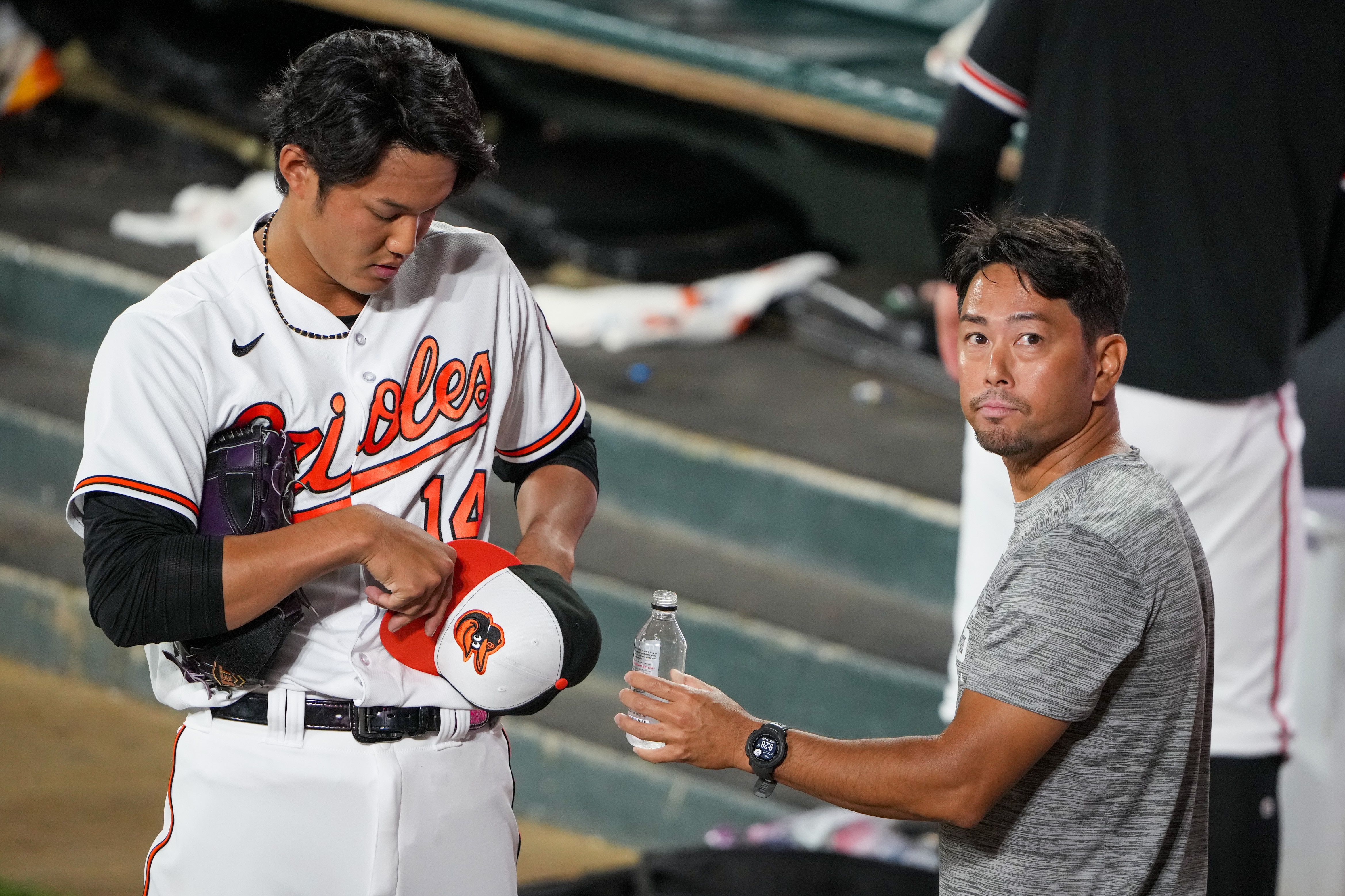 Baltimore Orioles relief pitcher Shintaro Fujinami (14) adjusts his hat as he talks with his interpreter, Issei Kamada, in the bullpen during a baseball game against the Houston Astros at Oriole Park at Camden Yards in Baltimore on Aug. 9, 2023.