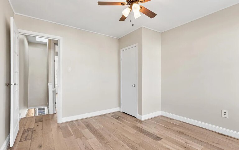 An upstairs bedroom with no furniture. There's hardwood floors with a light stain, beige walls and white trim.
