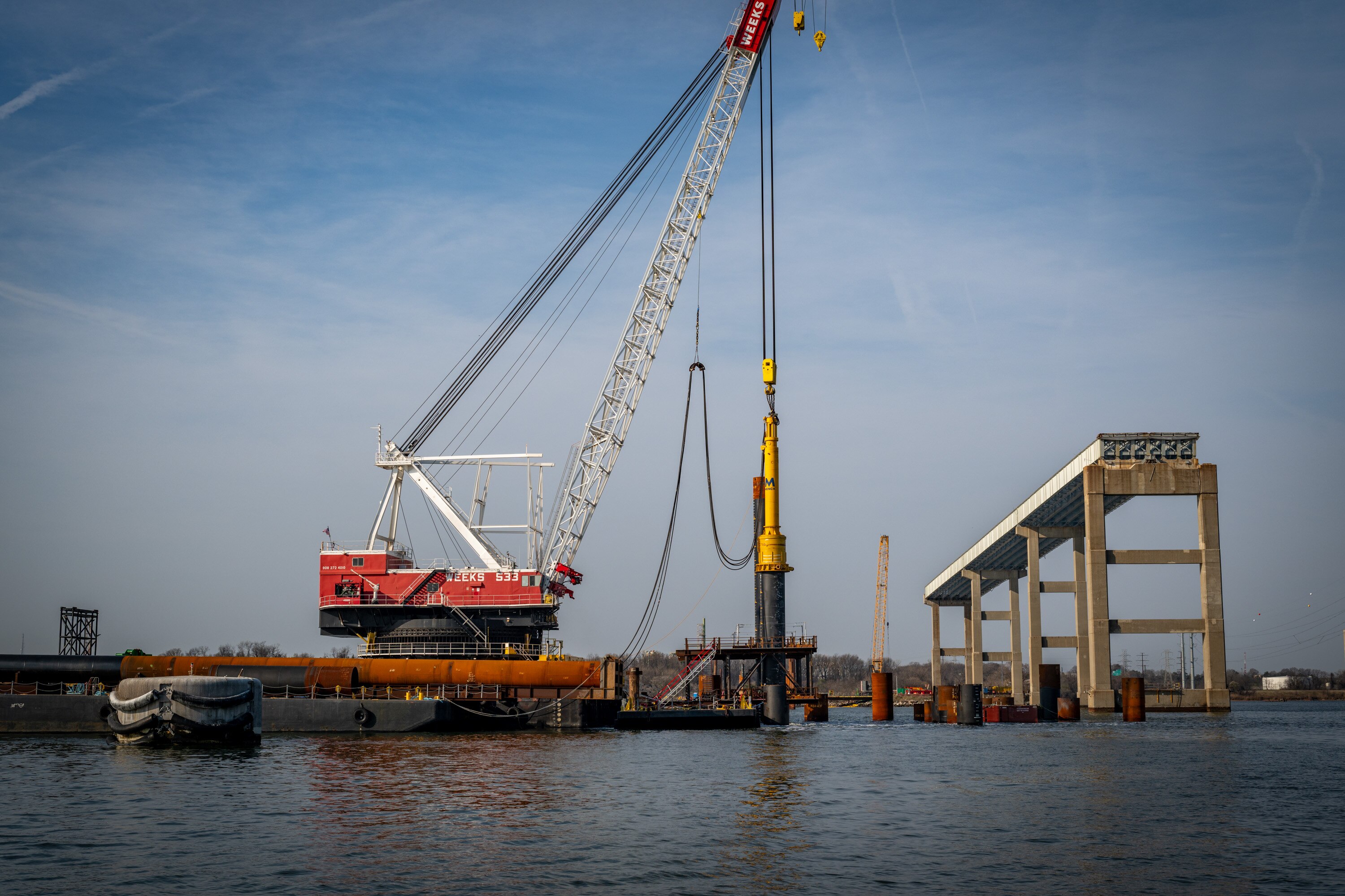 The Weeks 533 crane barge uses a pile driver to set a piling into the substrate below the Patapsco riverbed at the Francis Scott Key Bridge site.

