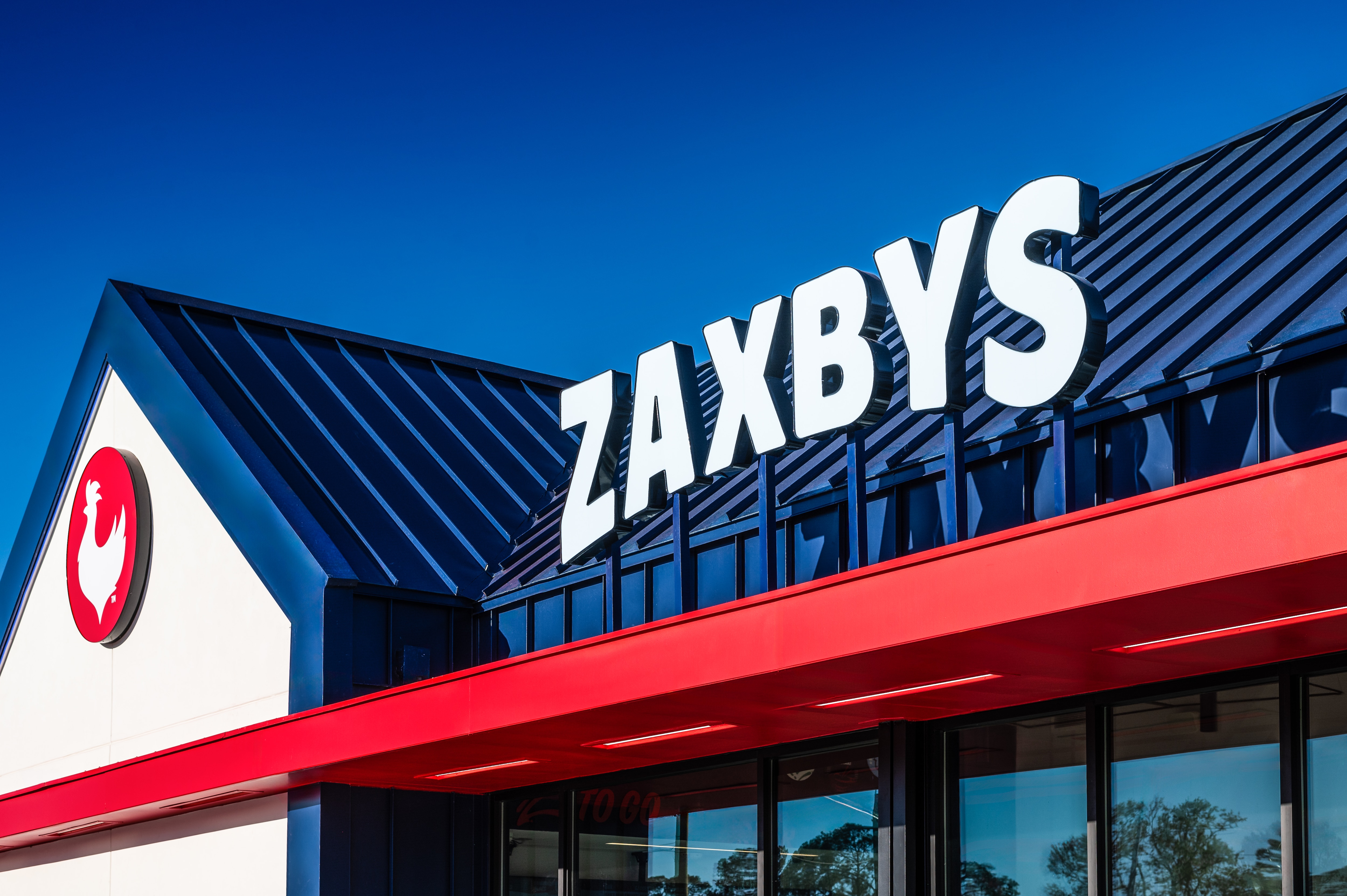 A white sign in all capital letters says "ZAXBYS" on top of a Zaxbys restaurant.