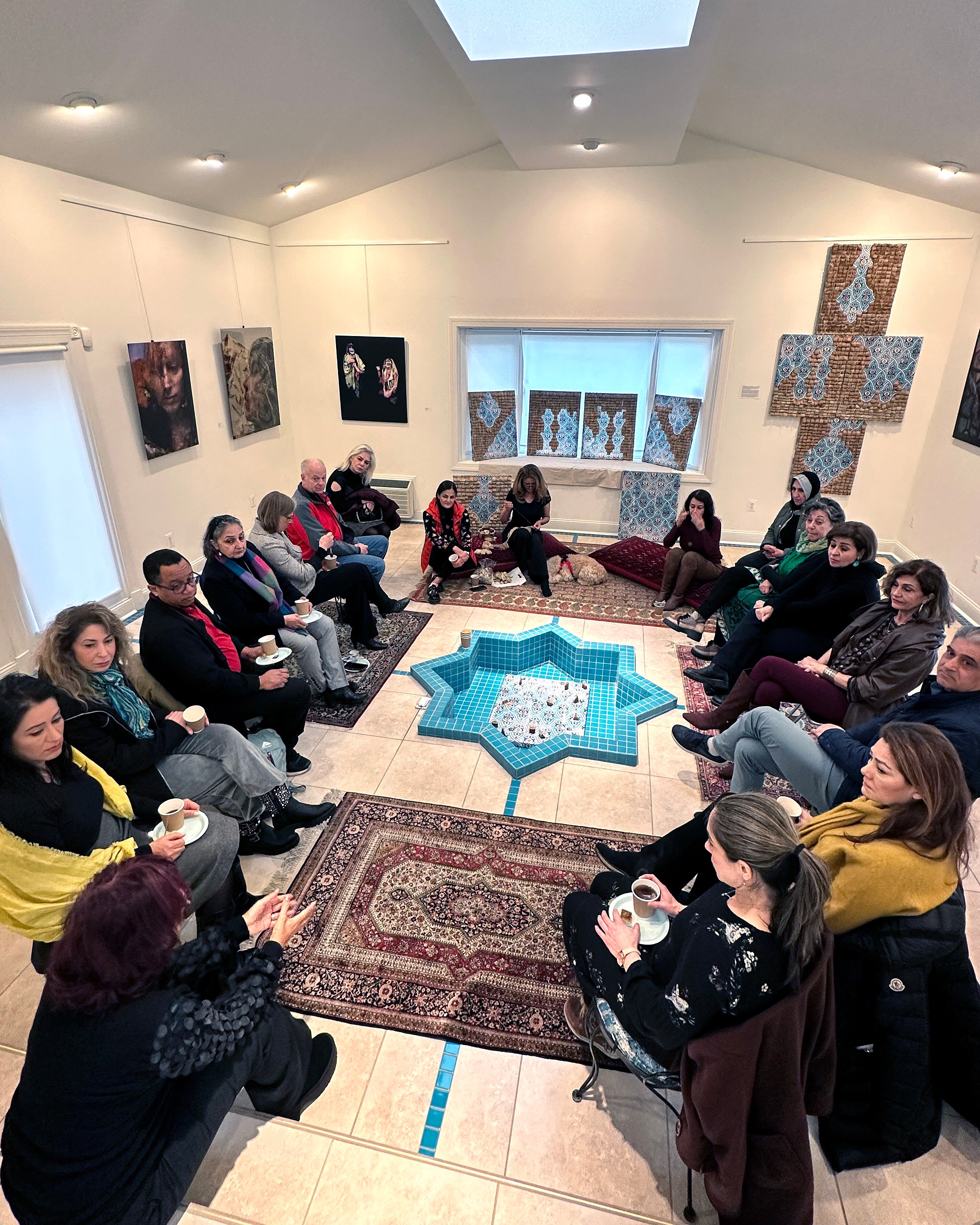 Phaedra Askarinam (back center) sews newly-donated used tea bags to her next creation while attendees share their fears about the war in Iran.