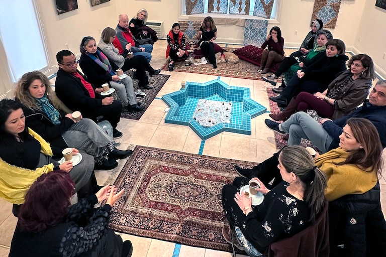 Phaedra Askarinam (back center) sews newly-donated used tea bags to her next creation while attendees share their fears about the war in Iran.