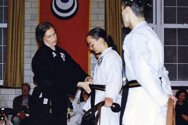 Carol Middleton helping a student tie their belt.