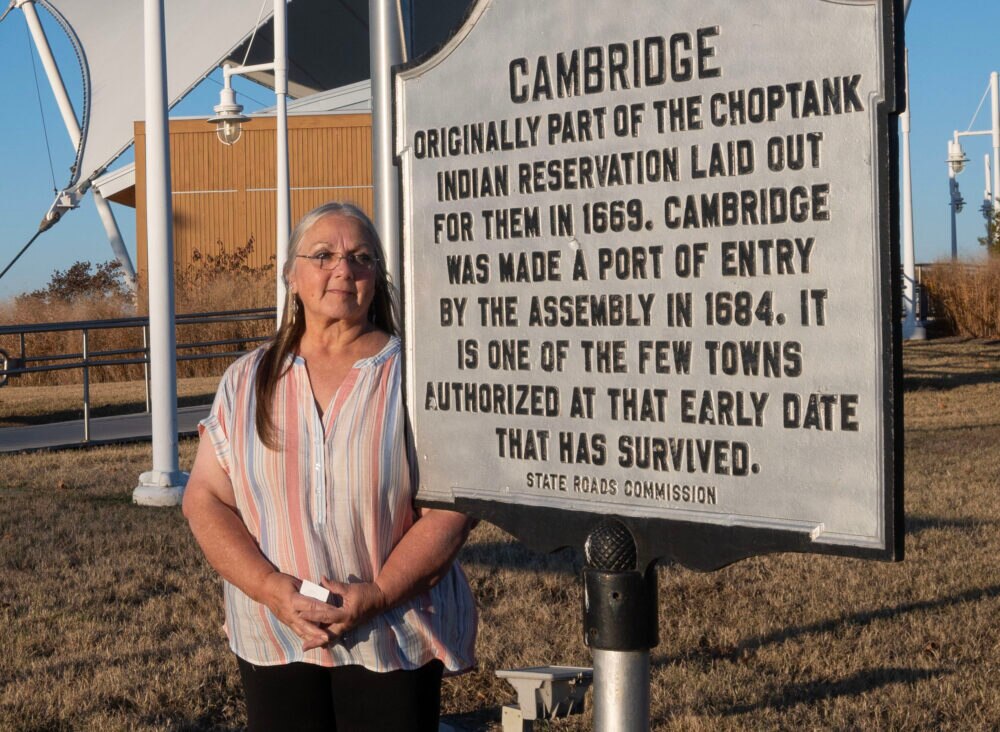 CAMBRIDGE, Md. - Nause-Waiwash Chief Donna Wolf Mother Abbott stands in front of the Dorchester County Visitor Center and the Cambridge land acknowledgment sign.
