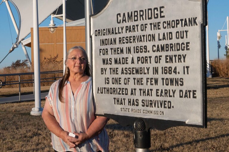 CAMBRIDGE, Md. - Nause-Waiwash Chief Donna Wolf Mother Abbott stands in front of the Dorchester County Visitor Center and the Cambridge land acknowledgment sign.