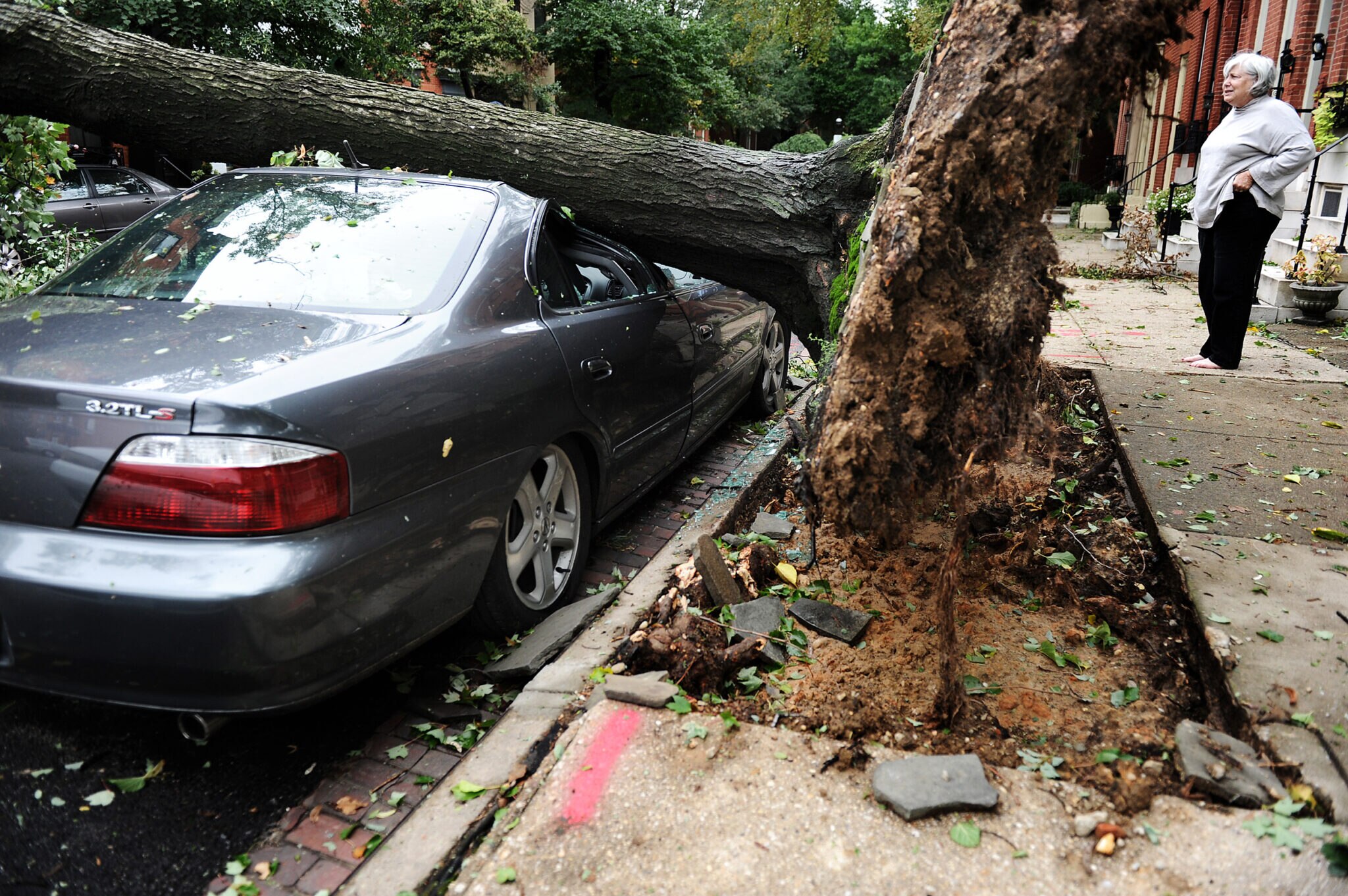 Passersby and neighbors look where a large tree crushed a car on Aug. 28, 2011, in Baltimore. Activists say climate change is producing larger, stronger storms.