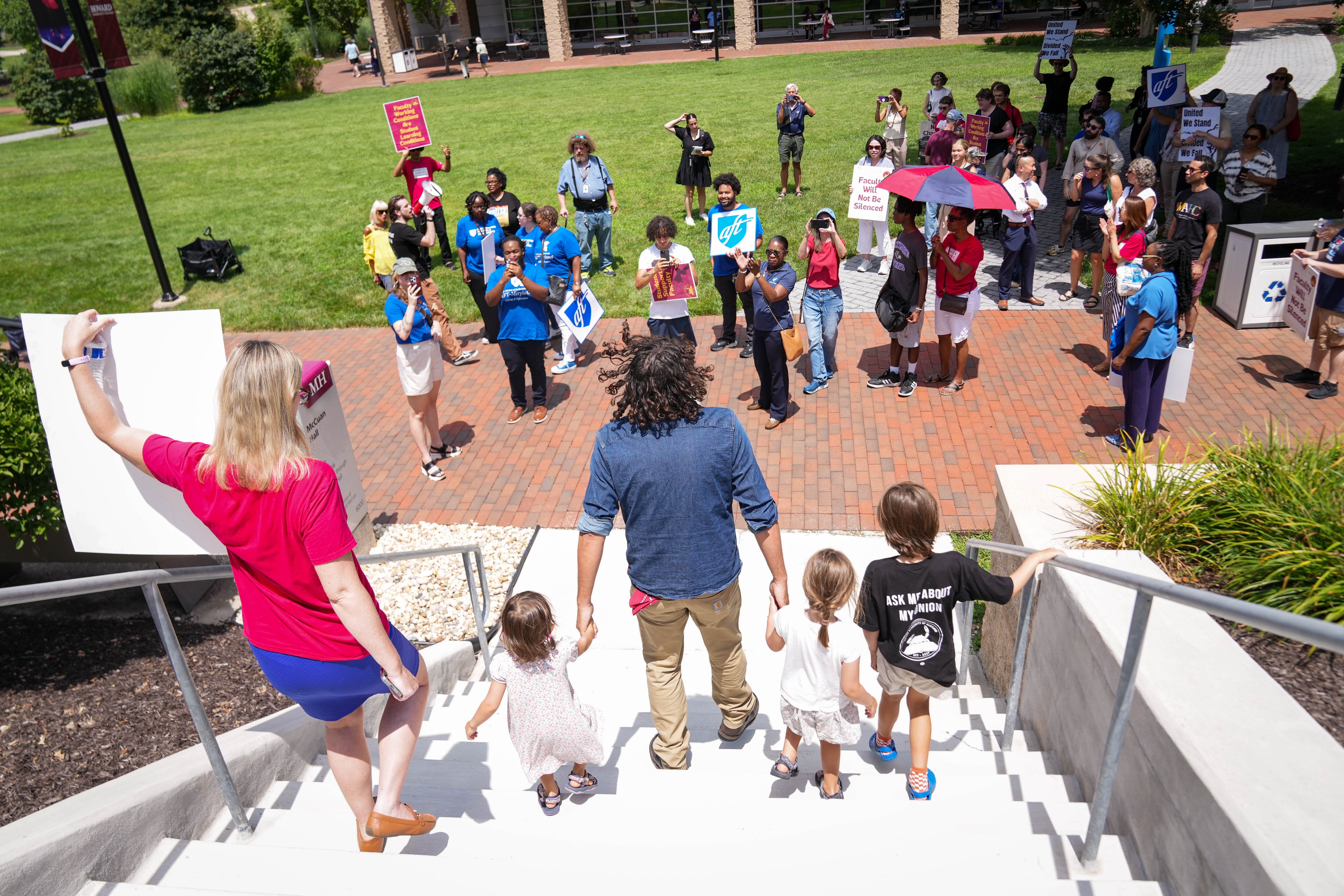 Dr. Alejandro Muzzio, an HCC faculty member, holds the hands of his children after delivering a list of the faculty’s demands of the HCCC administration following a rally to support Howard Community College faculty on the school’s quad in Columbia, Md. on Monday, July 28, 2025.