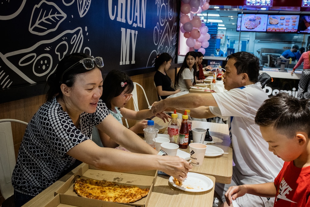 Dong Nai, Vietnam - Aug 2, 2026: Danny Hoang, 56, and Melissa Tran, 44, help their children, Jacob and Riley, as they eat pizza at Dominos in Dong Nai, Vietnam on August 2, 2026. Rosem Morton for The Baltimore Banner