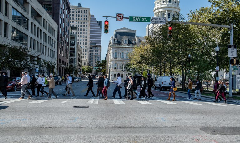 A group of people cross a downtown street on a bright, sunny day.